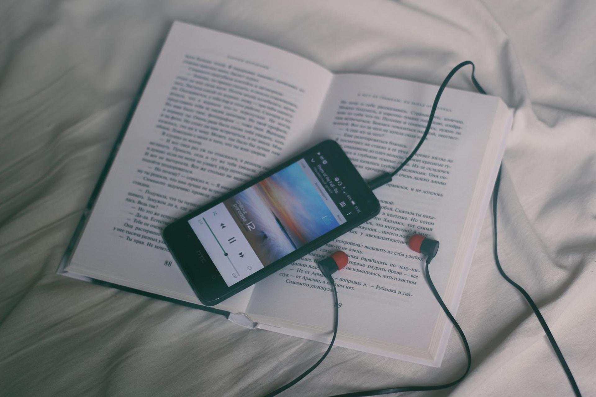 An open book with a phone playing an audiobook laying on top