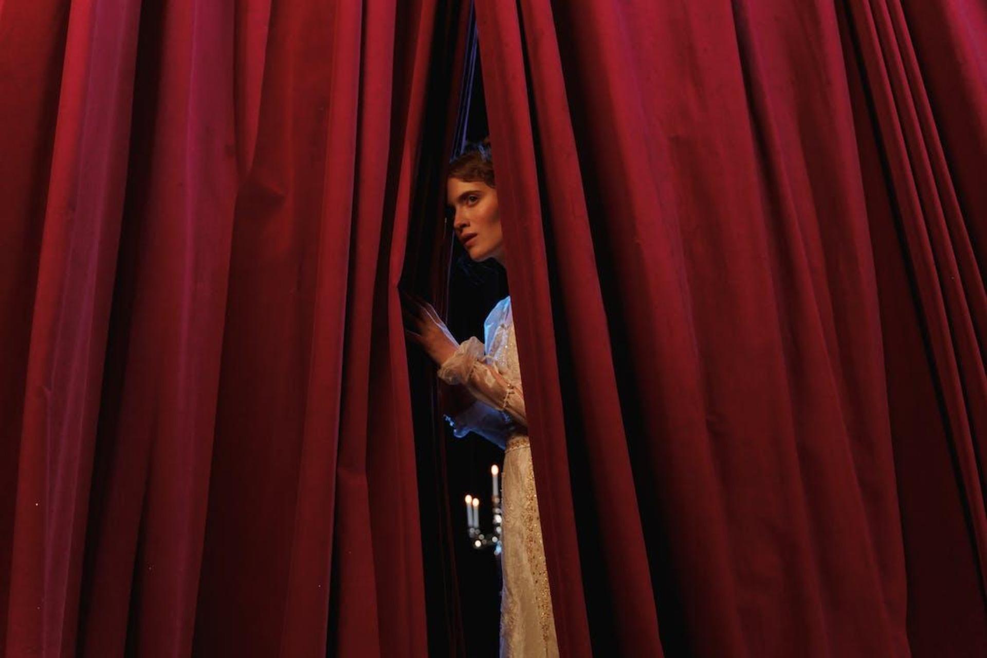 A woman standing behind a red curtain.