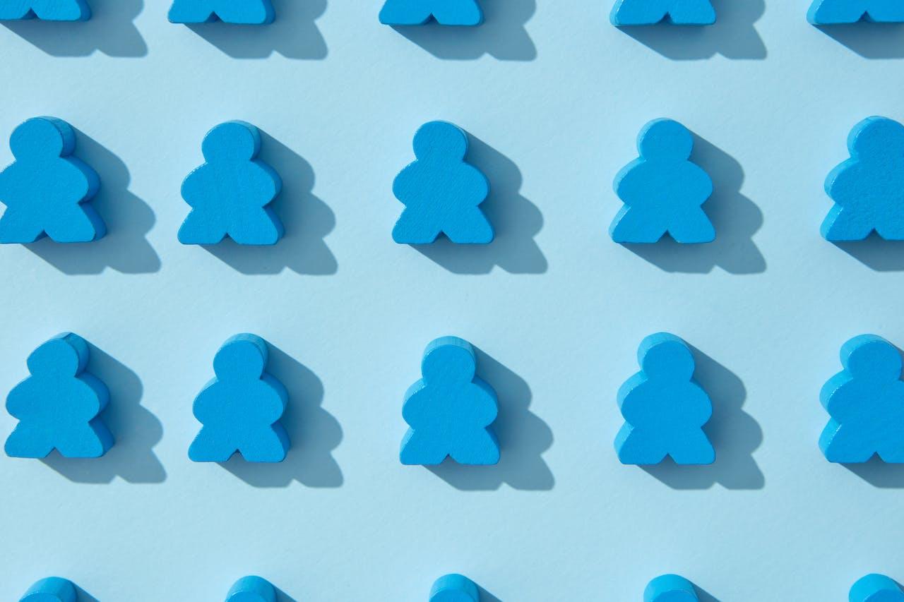 Blue wooden blacks shaped like people making a repetitive pattern against a lighter blue background