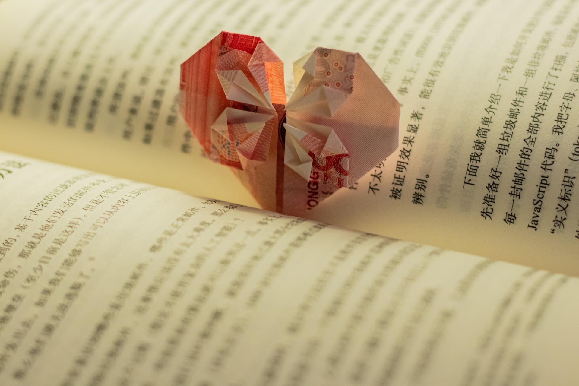 An open book written in Chinese with an origami heart standing in its spine, folded out of a 100 yuan bill.