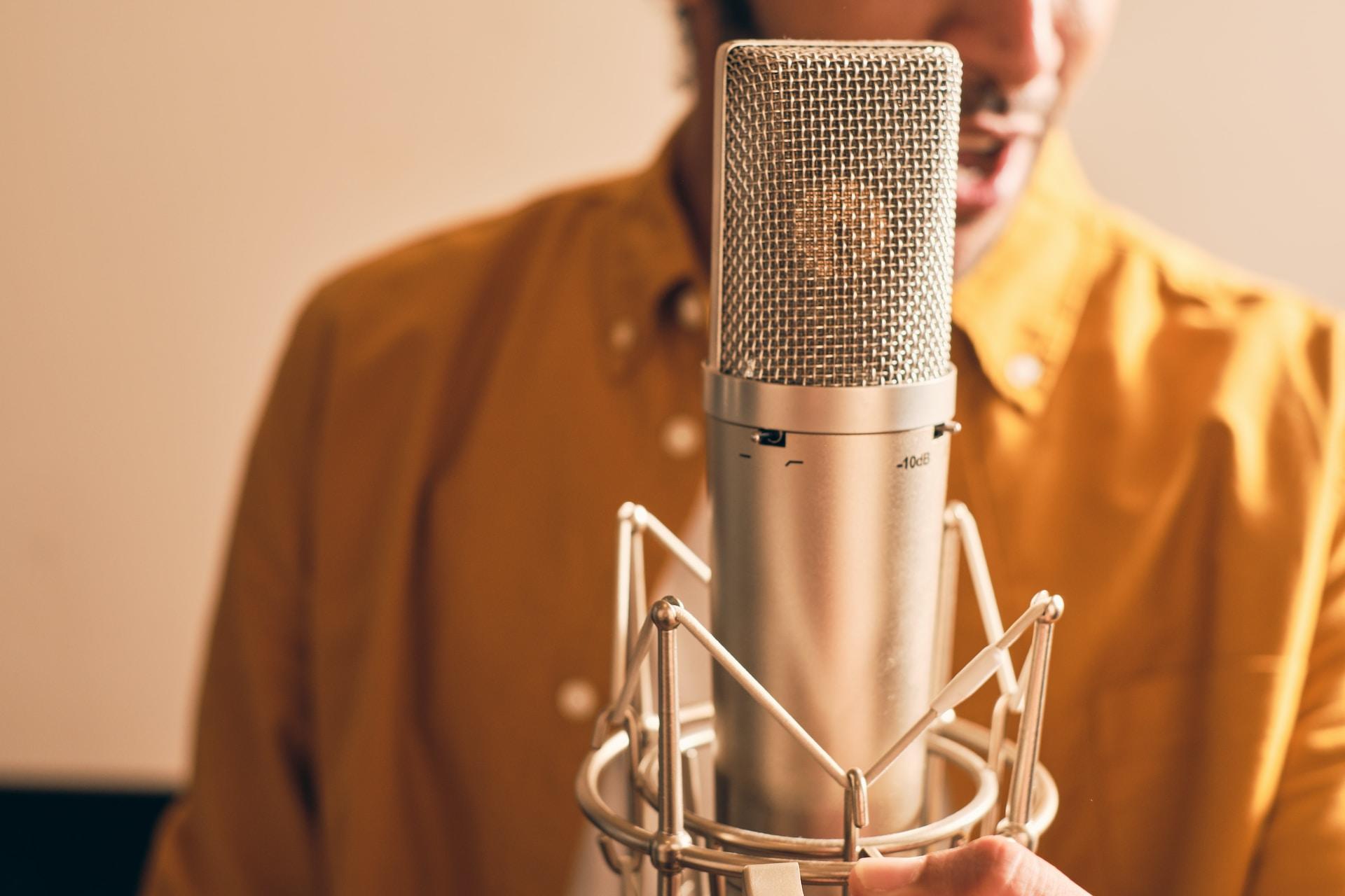 Close-up of a professional microphone against the blurred background of a person in a mustard-colored shirt, symbolizing the preparation and care behind every powerful vocal performance.