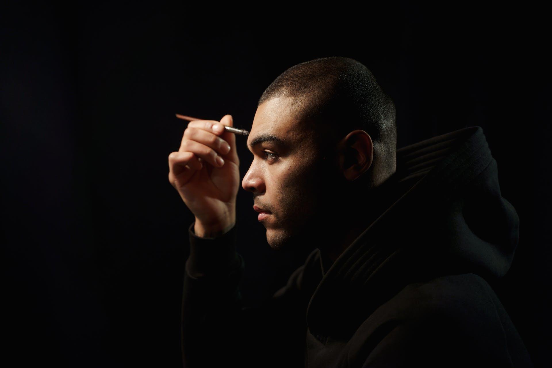 A male actor carefully applying makeup to his face, concentrating on the details, as he prepares for a performance after an audition.