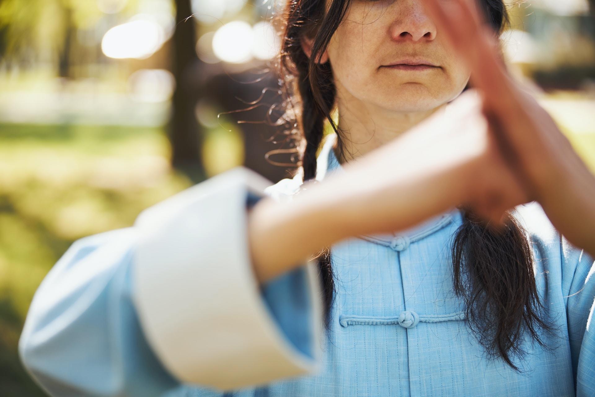 A person in a light blue tongzuang holds their fisted right hand in their open left palm as a sign of respect.