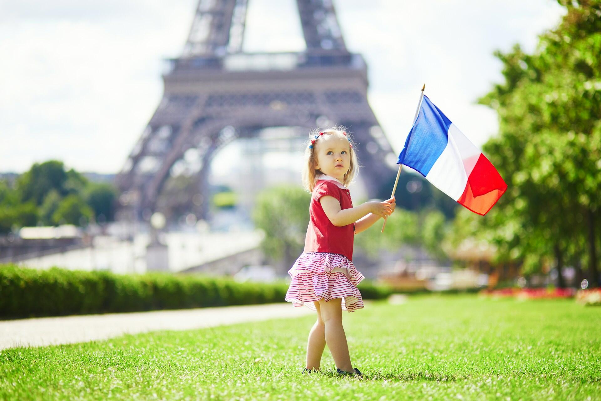 A child holds a French flag in front of the Eiffel Tower. 