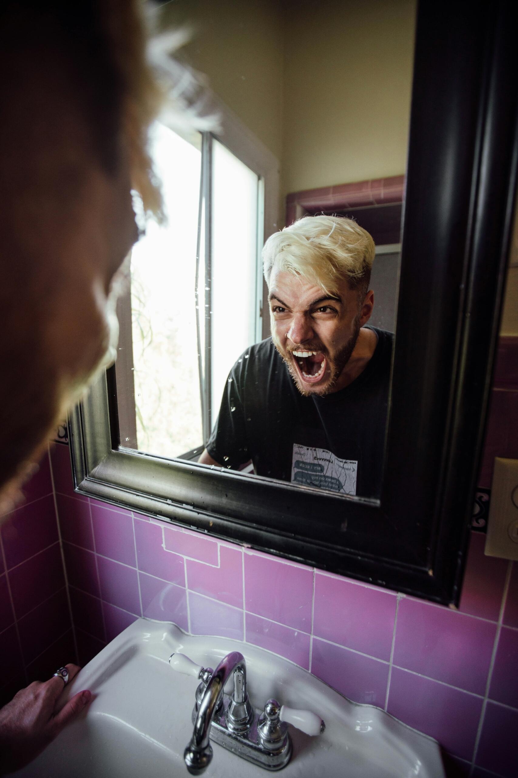 A person looking in the mirror with an enraged expression on their face. 