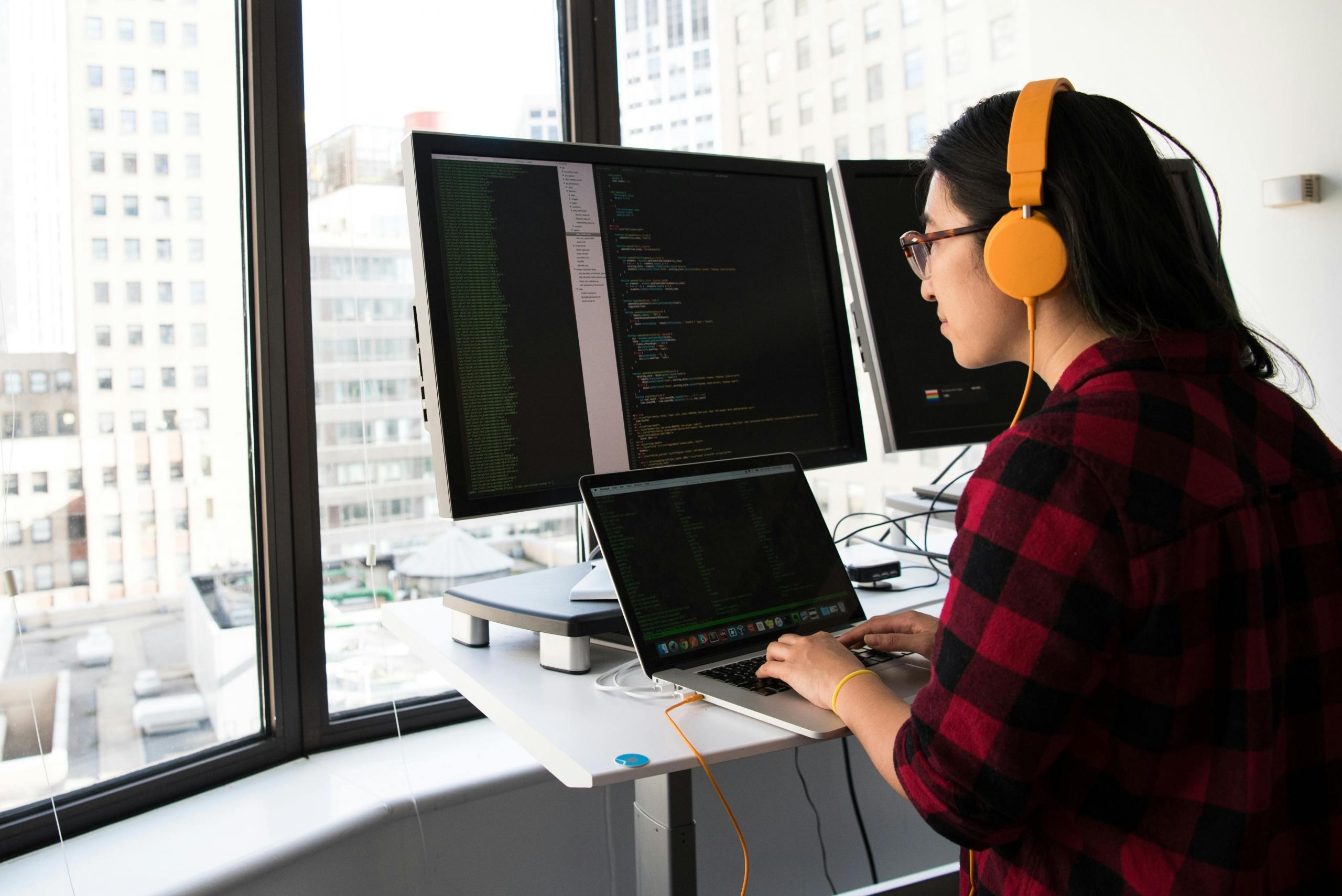 A programmer working at home on his laptop with a computer monitor as well. 