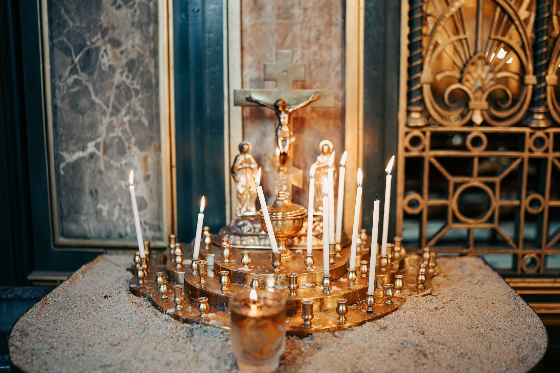 Ornamental candles in a church, some lit, some not, with a crucifix in the background.