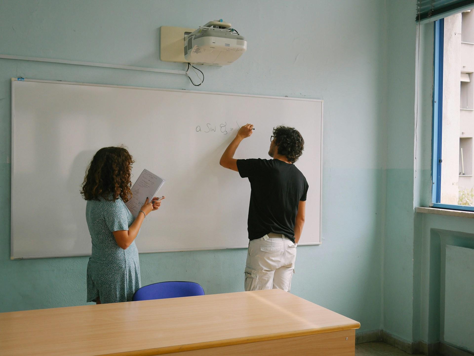 A student showing his teacher his working on a white board.