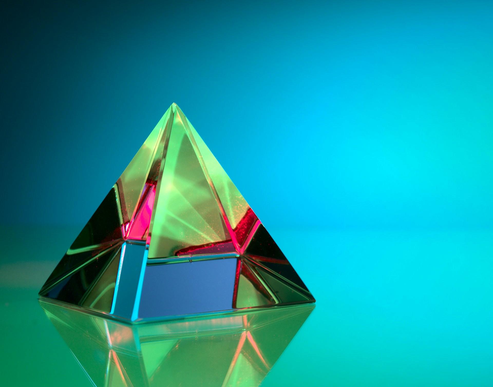 A multicoloured prism resting on a mirrored surface which reflects the image's greenish tone.