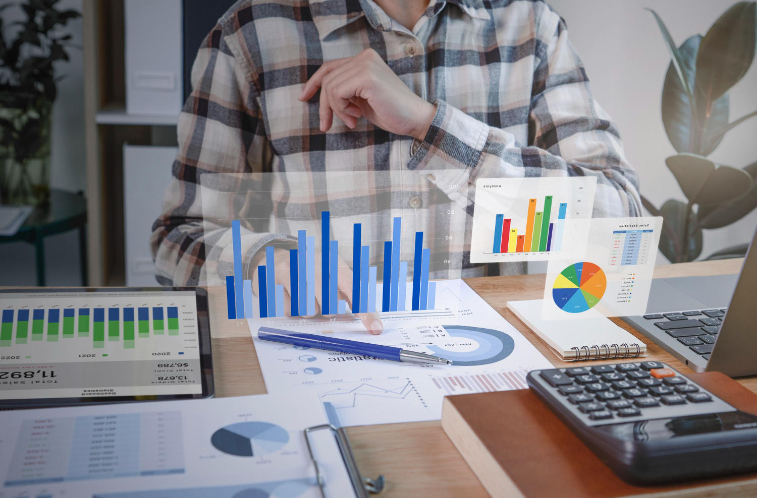 A graphic with charts and graphs hovering in front of a person making spreadsheets.