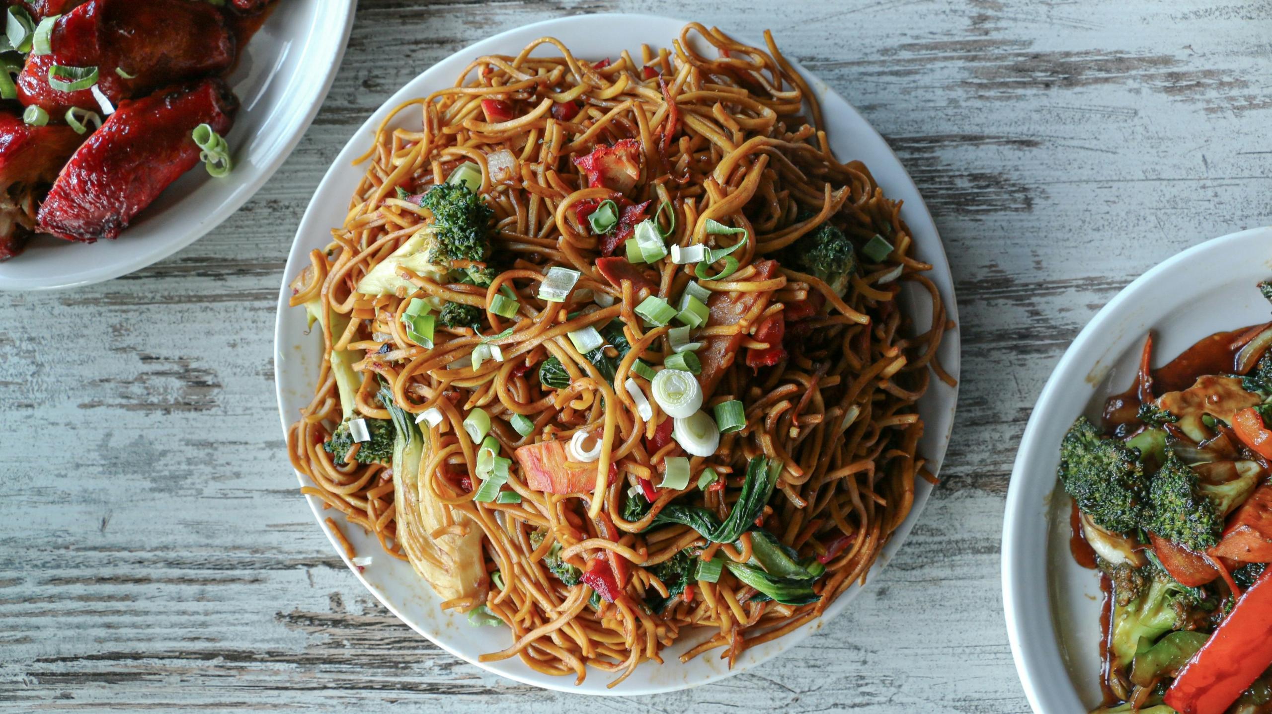 A picture of chow mein with 2 other chinese dishes.