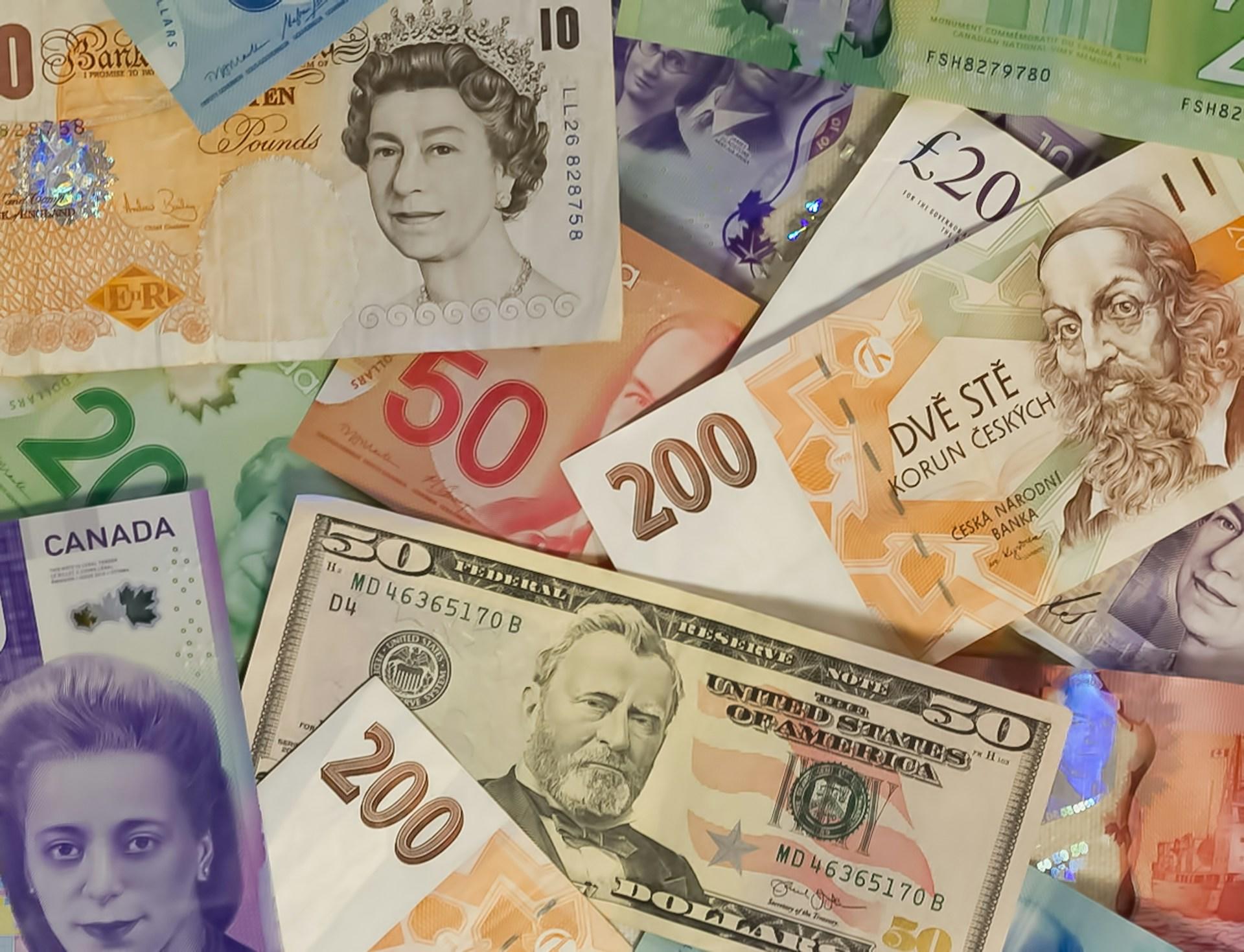 A scattering of world currencies featuring an orange and whit £10 note, a $50 bill and a purple Canadian bill.