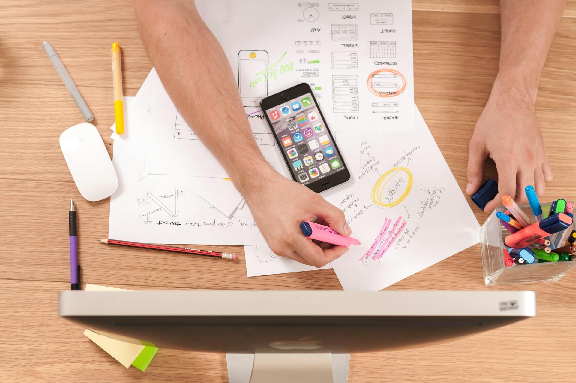 A person with lots of papers and data in a mess on their desk as they highlight things.