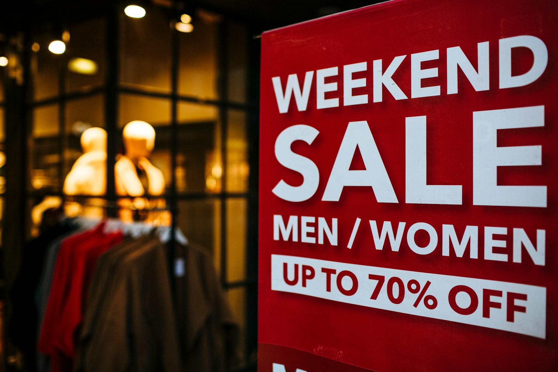 A large red sign with white lettering that announces a weekend sale contrasts against the nighttime environment.