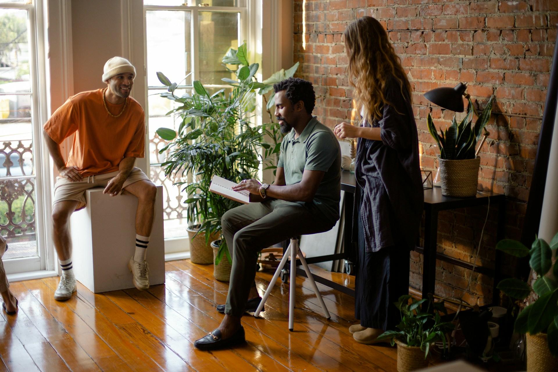 A group of people lounge around an attractive space that features gleaming wooden floors, plants and a brick wall, which forms the backdrop of the image.