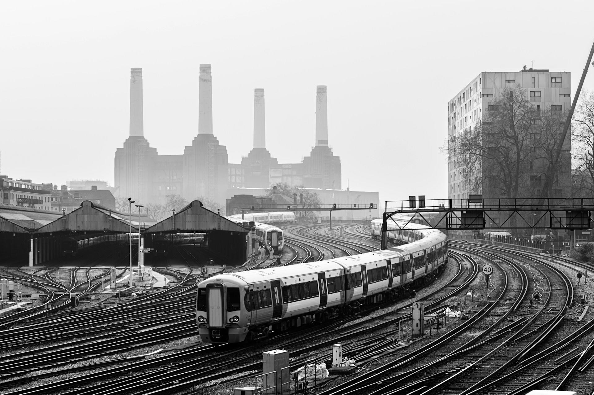 A greyscale image of a train passing in front of Battersea power station in London on a smoggy day. 
