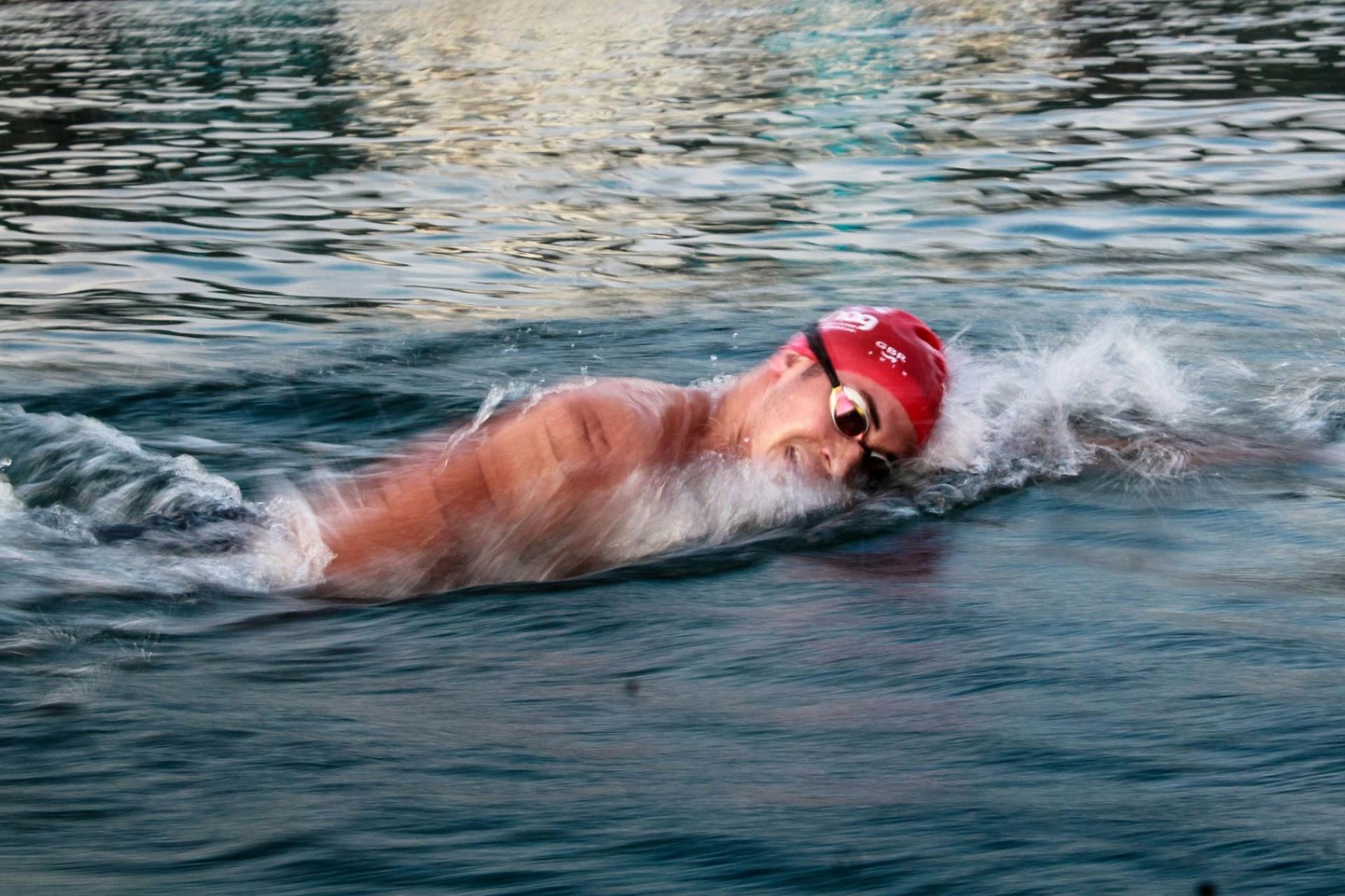 A man in a swim cap and goggles swimming outdoors.