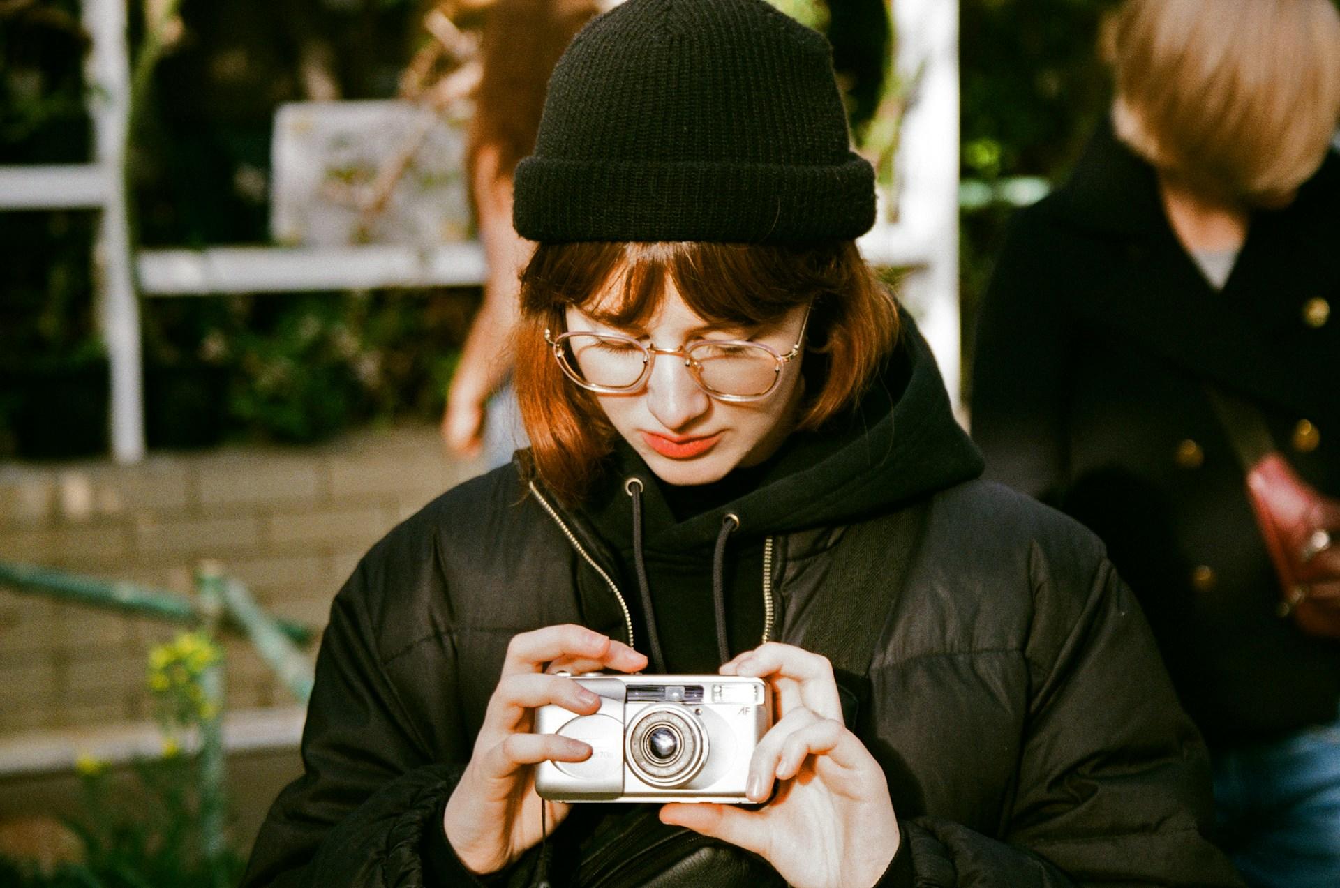 A person wearing a black beanie and jacket holds a vintage film camera.