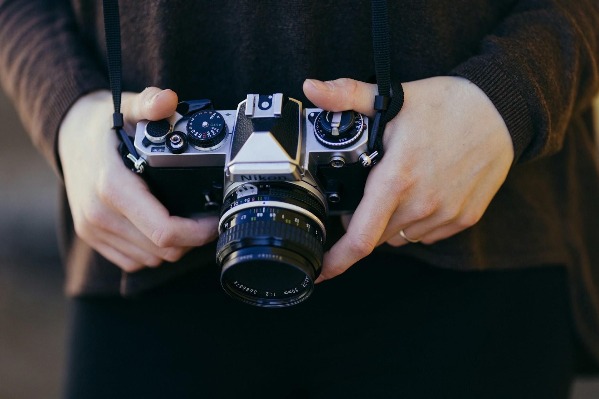 A person holds a vintage Nikon SLR camera with a black lens.