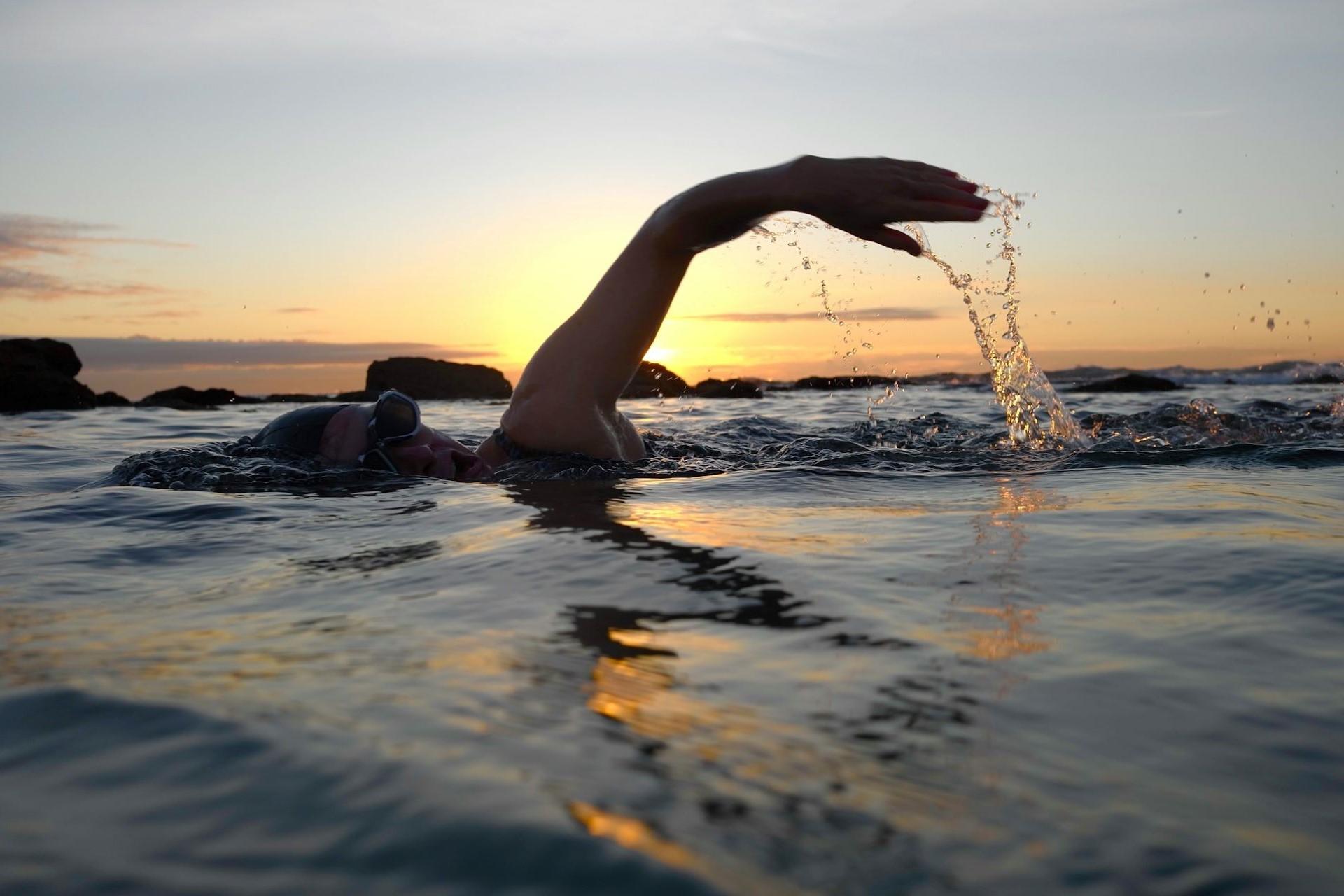 A person swimming outdoors at sunrise.