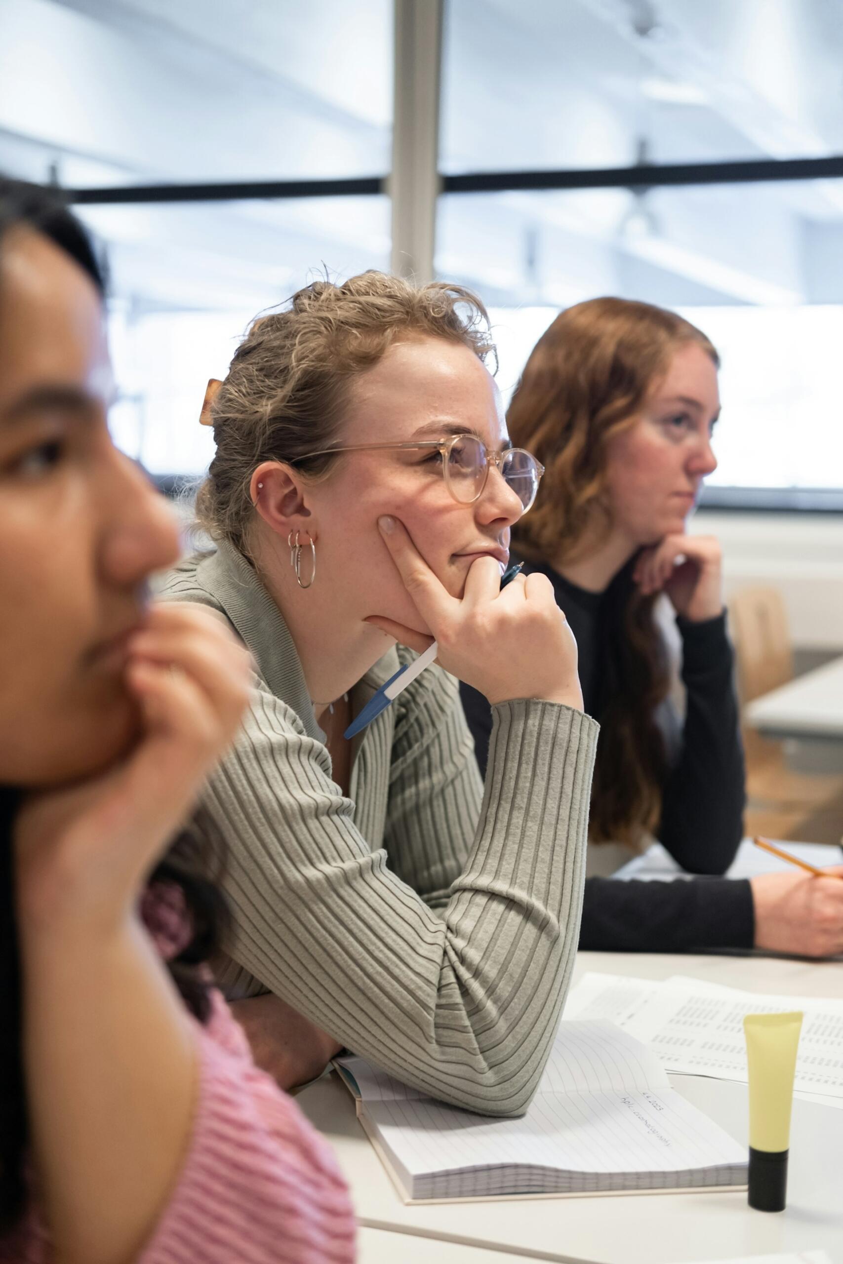 Three people in a classoom, listening.