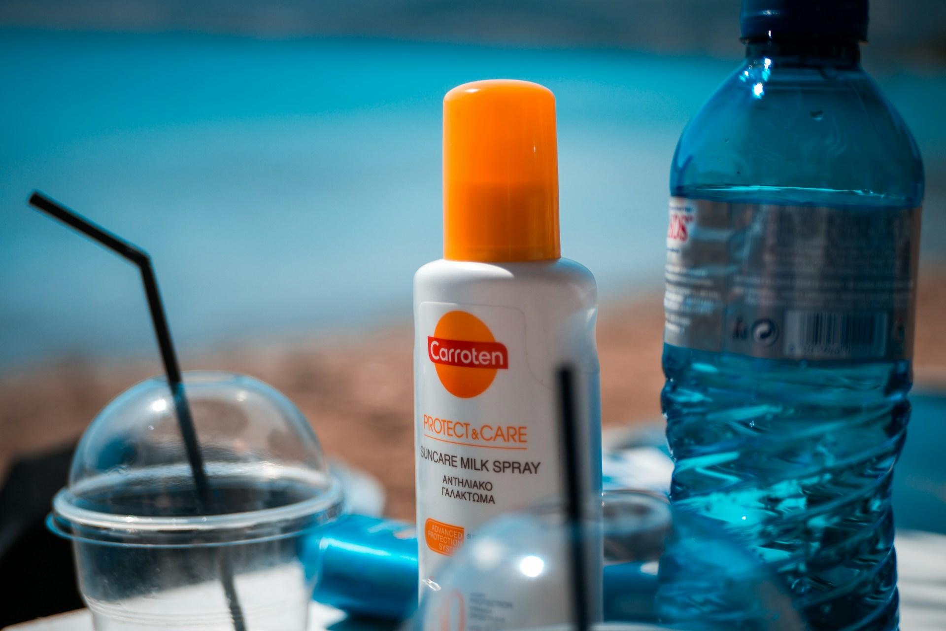 A bottle of sunscreen next to a drink and a bottle of water.
