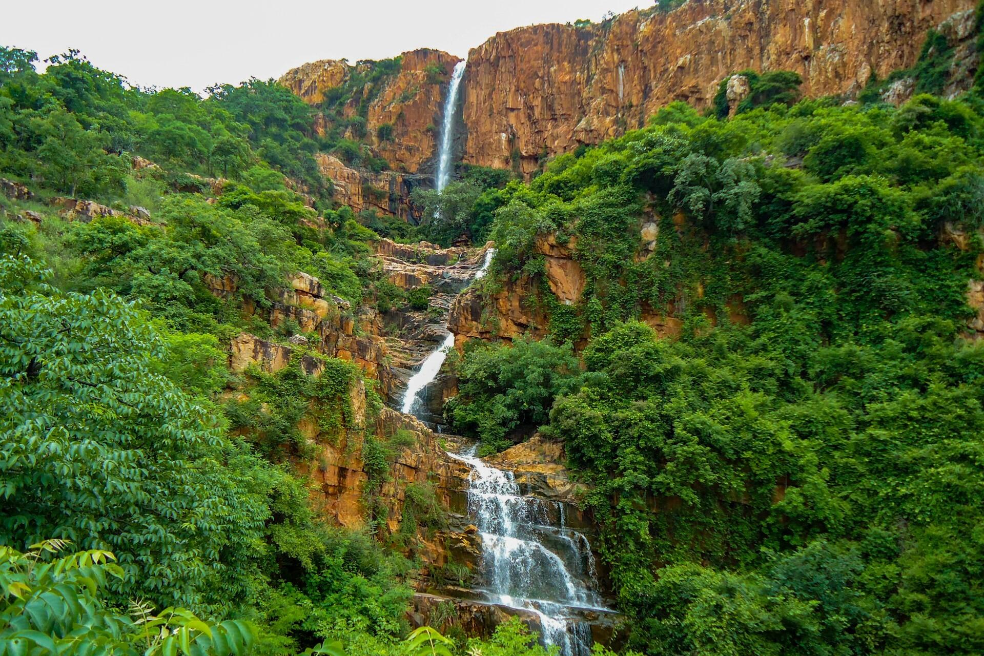 Waterfall cascading down rocky cliffs surrounded by dense green vegetation