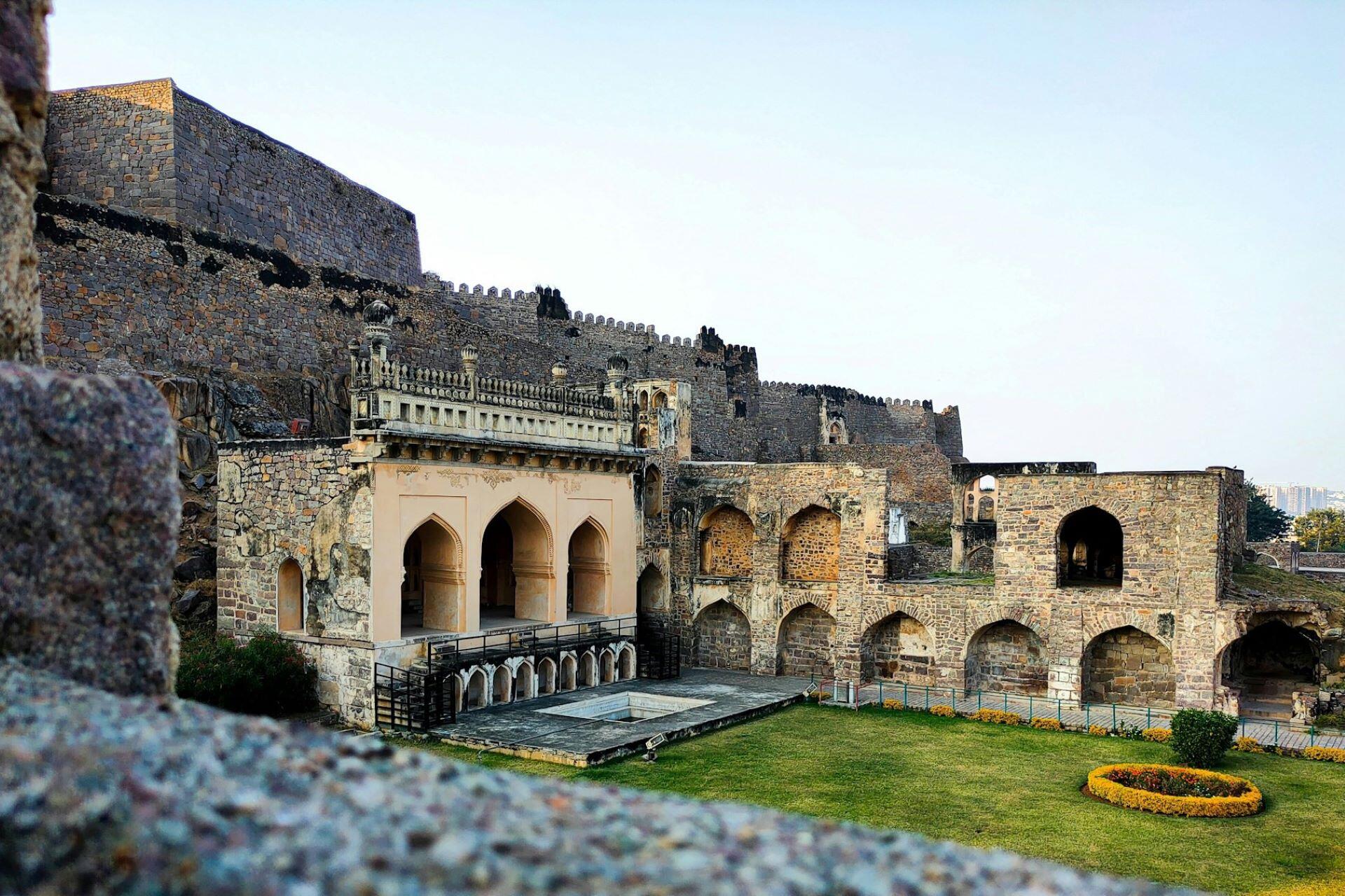 Stone fort walls and arched buildings surrounding a grassy courtyard