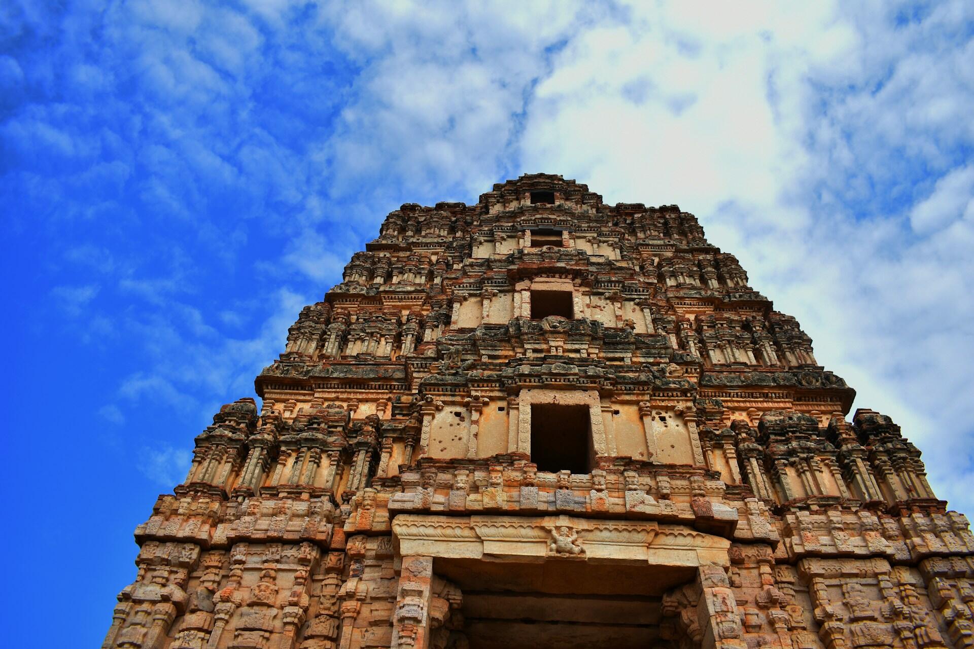 Ornately carved historic tower viewed from below against a blue and cloudy sky