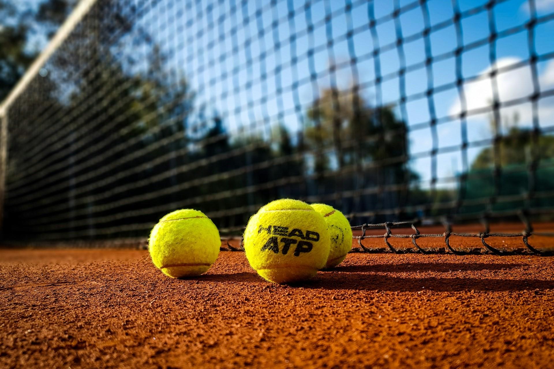 Some tennis balls on a clay court by the net.