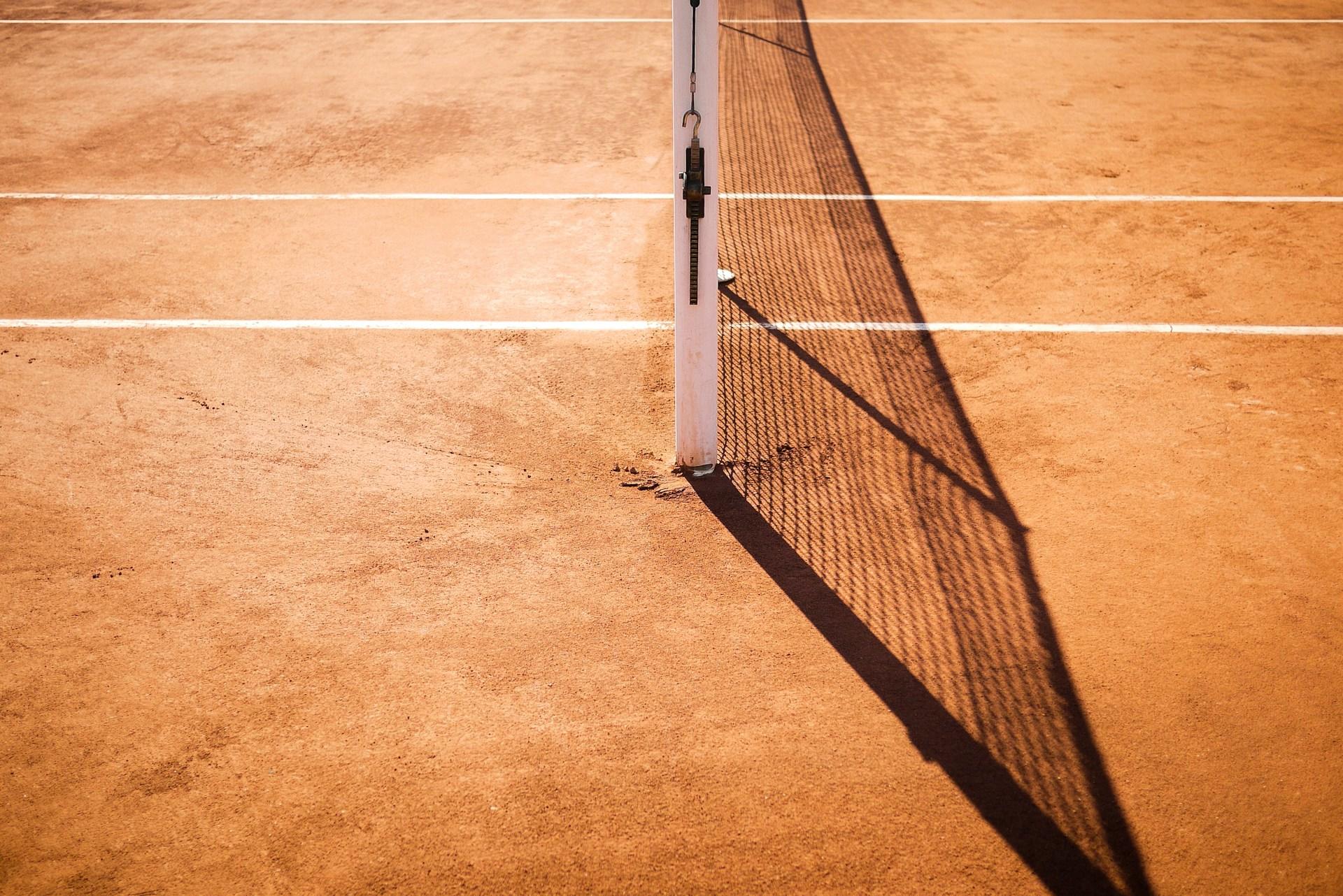 A closeup of a tennis net on a clay court.