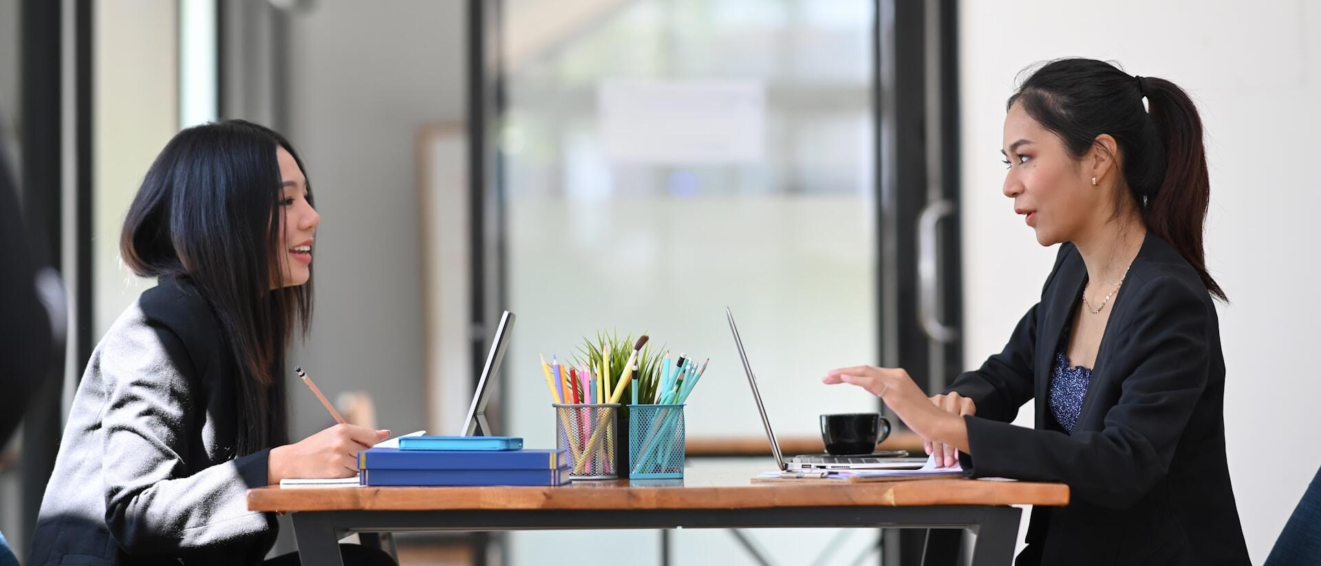 Two women across the table from each other, with books and a computer open between them.