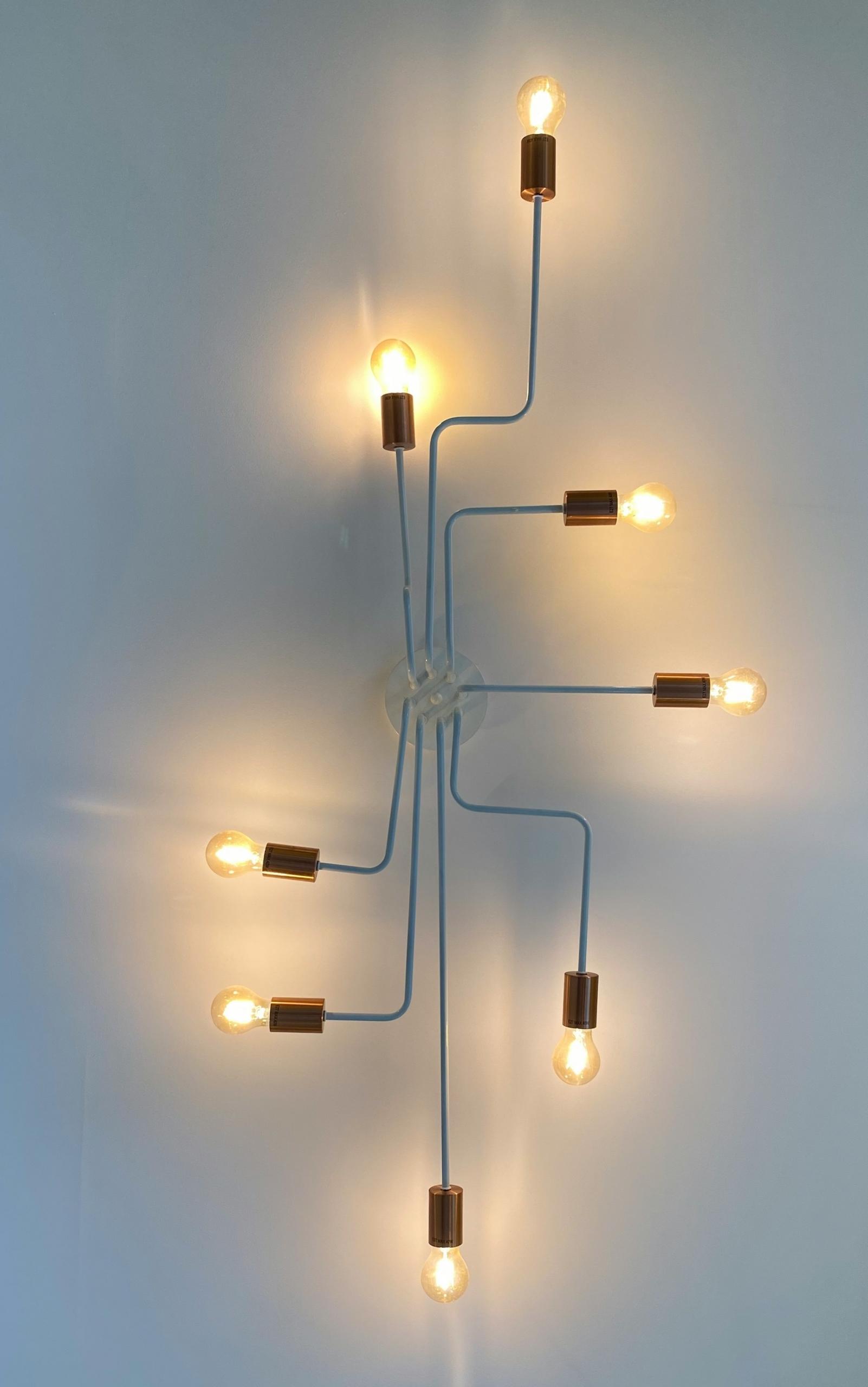 A wall mounted light fixture featuring eight thin blue arms that terminate in a brass socket, each with a lit bulb. 