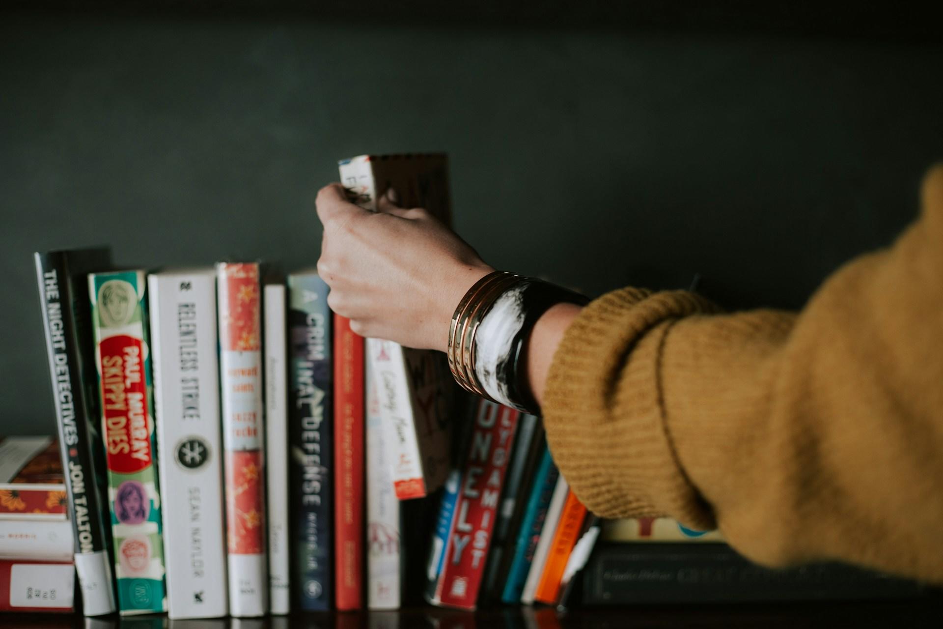 Person removing a book from a book shelf.
