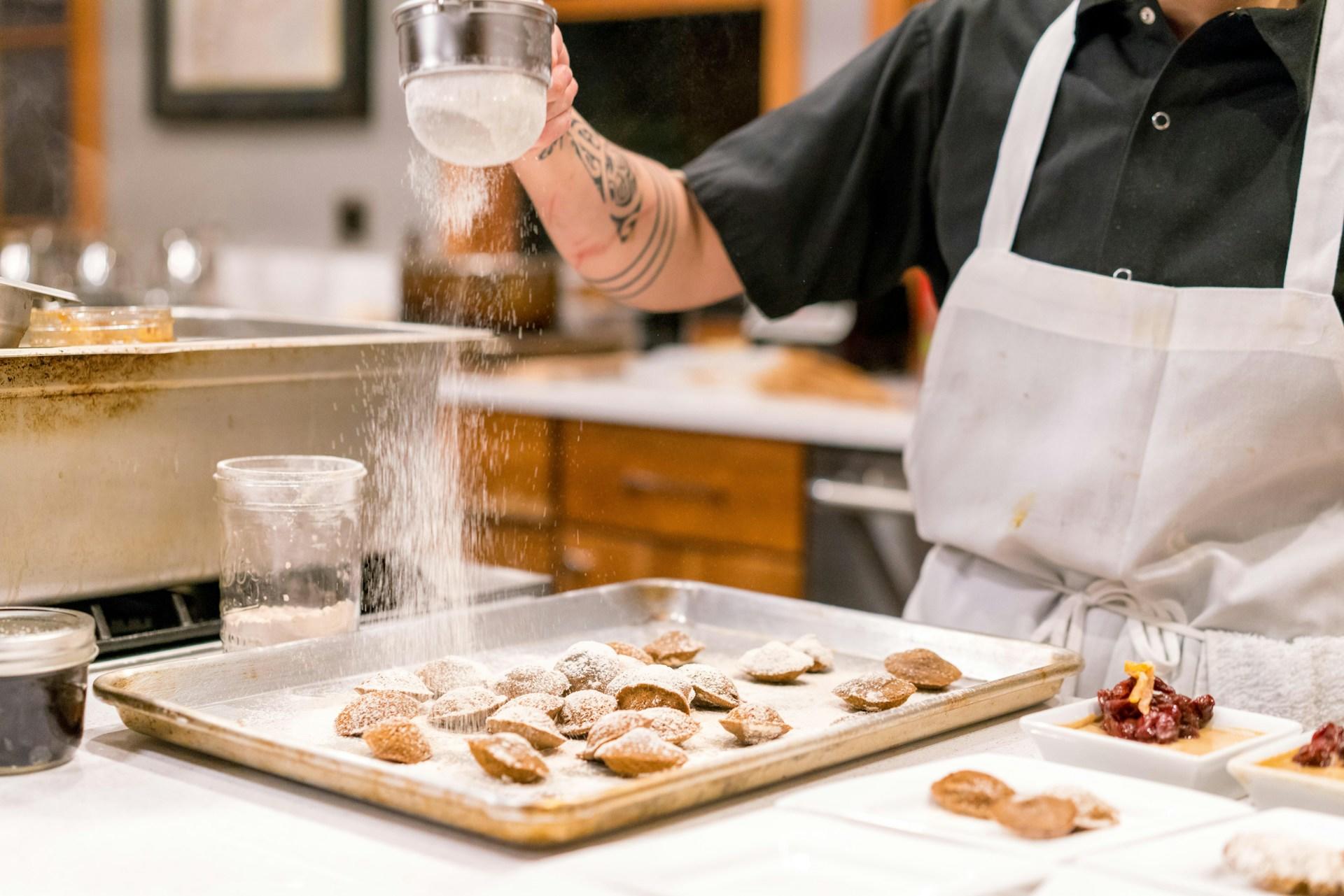 A chef putting white sugar on top of pastries.