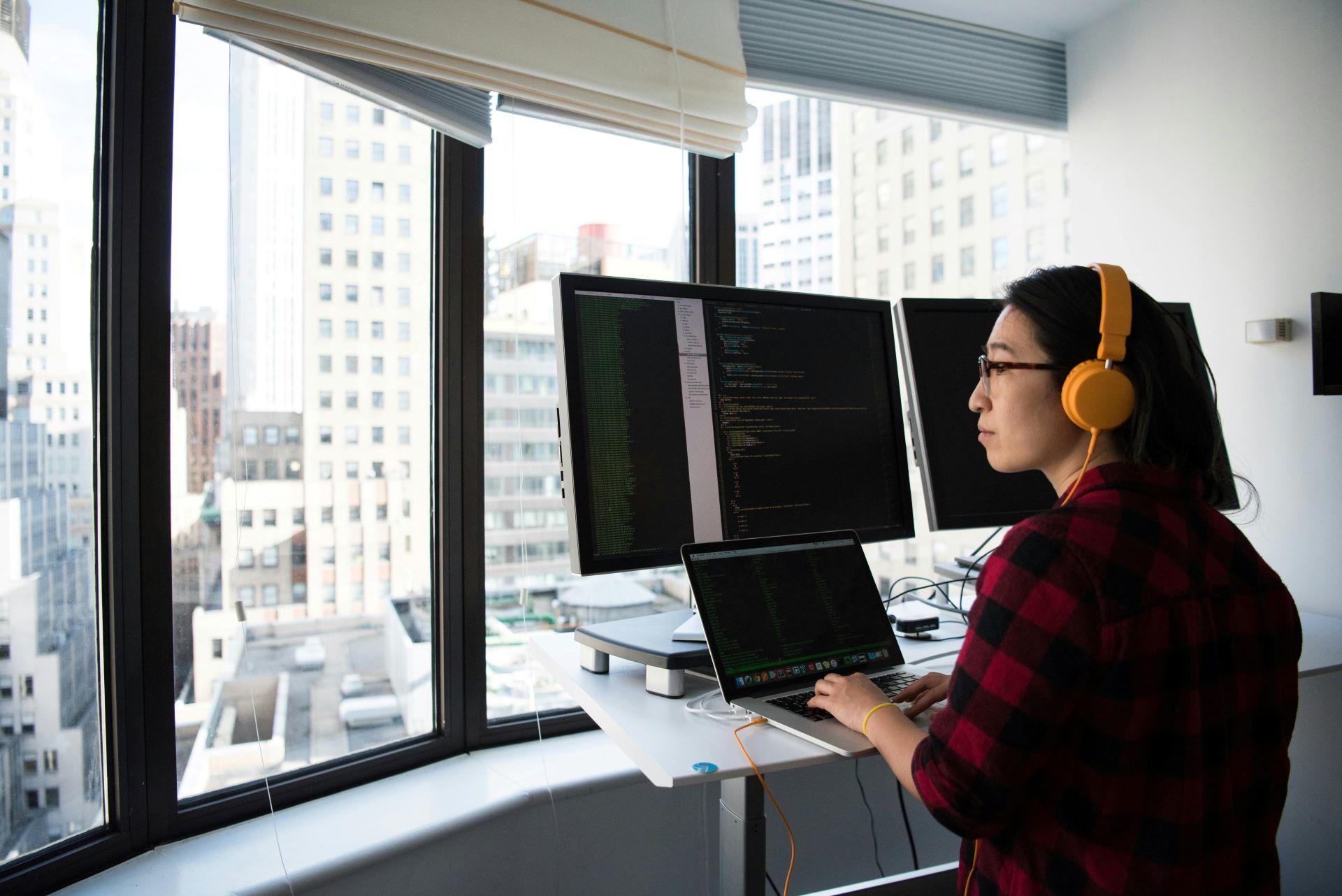 A woman wearing headphones types code on a laptop.