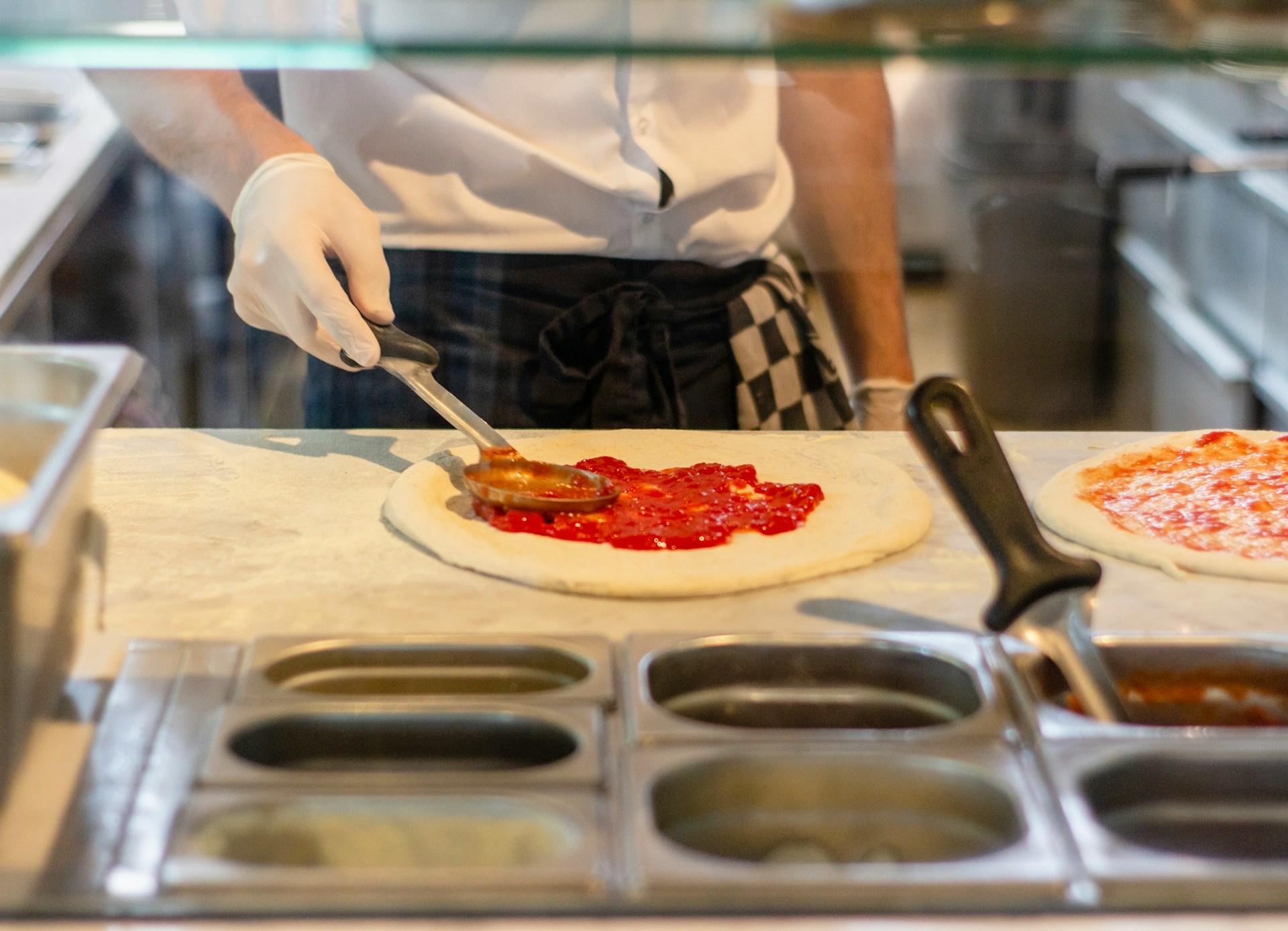 a chef preparing a pizza by adding tomato sauce to the pizza dough.