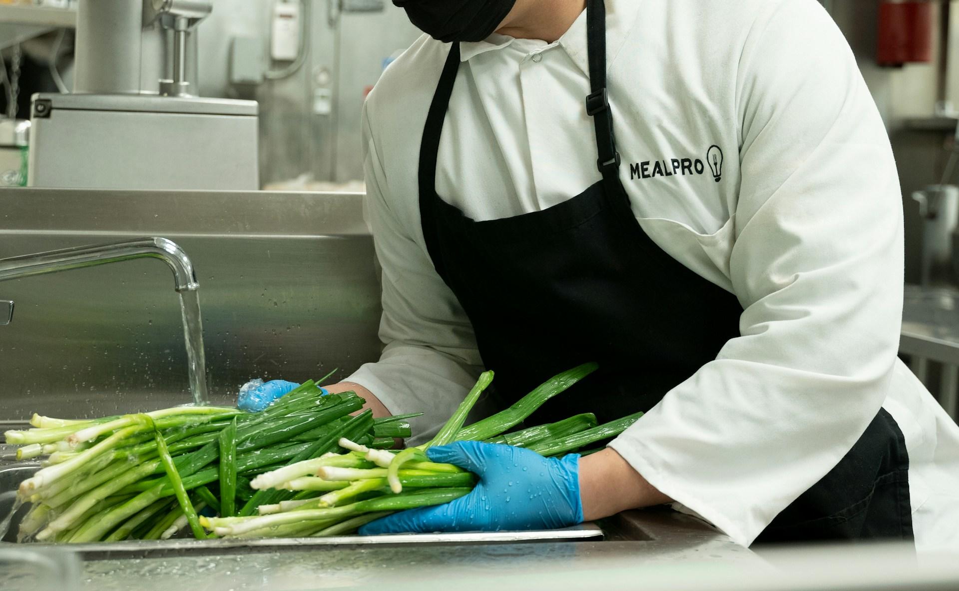 A chef washing and preparing spring onion for a meal.