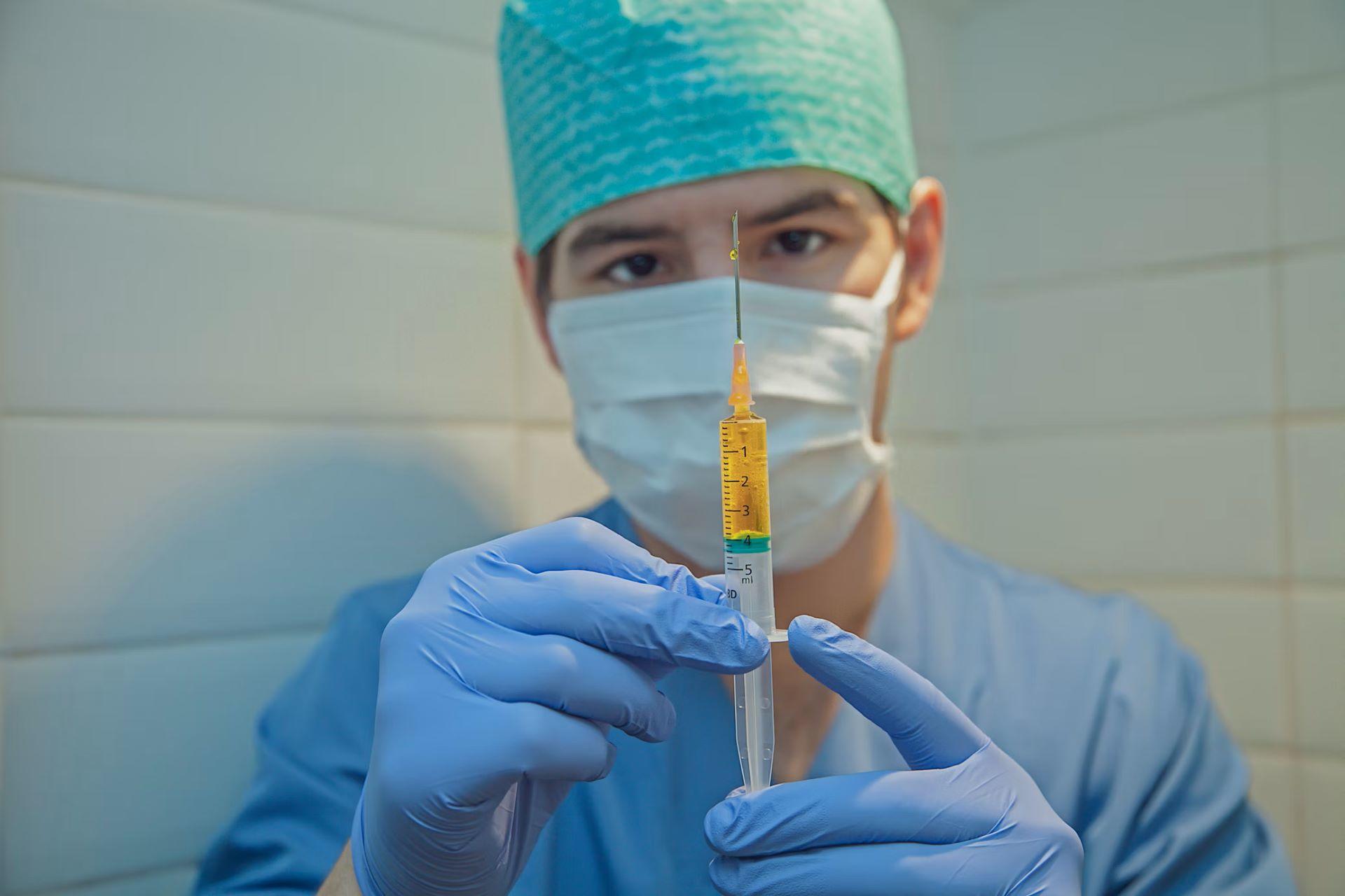 A man in gloves holding a syringe filled with yellow liquid.