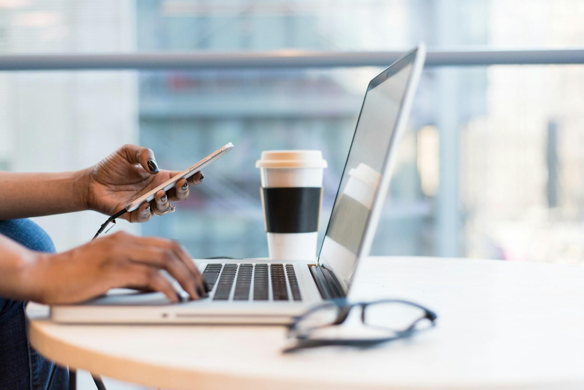 A person dials a phone while sitting in front of their computer.