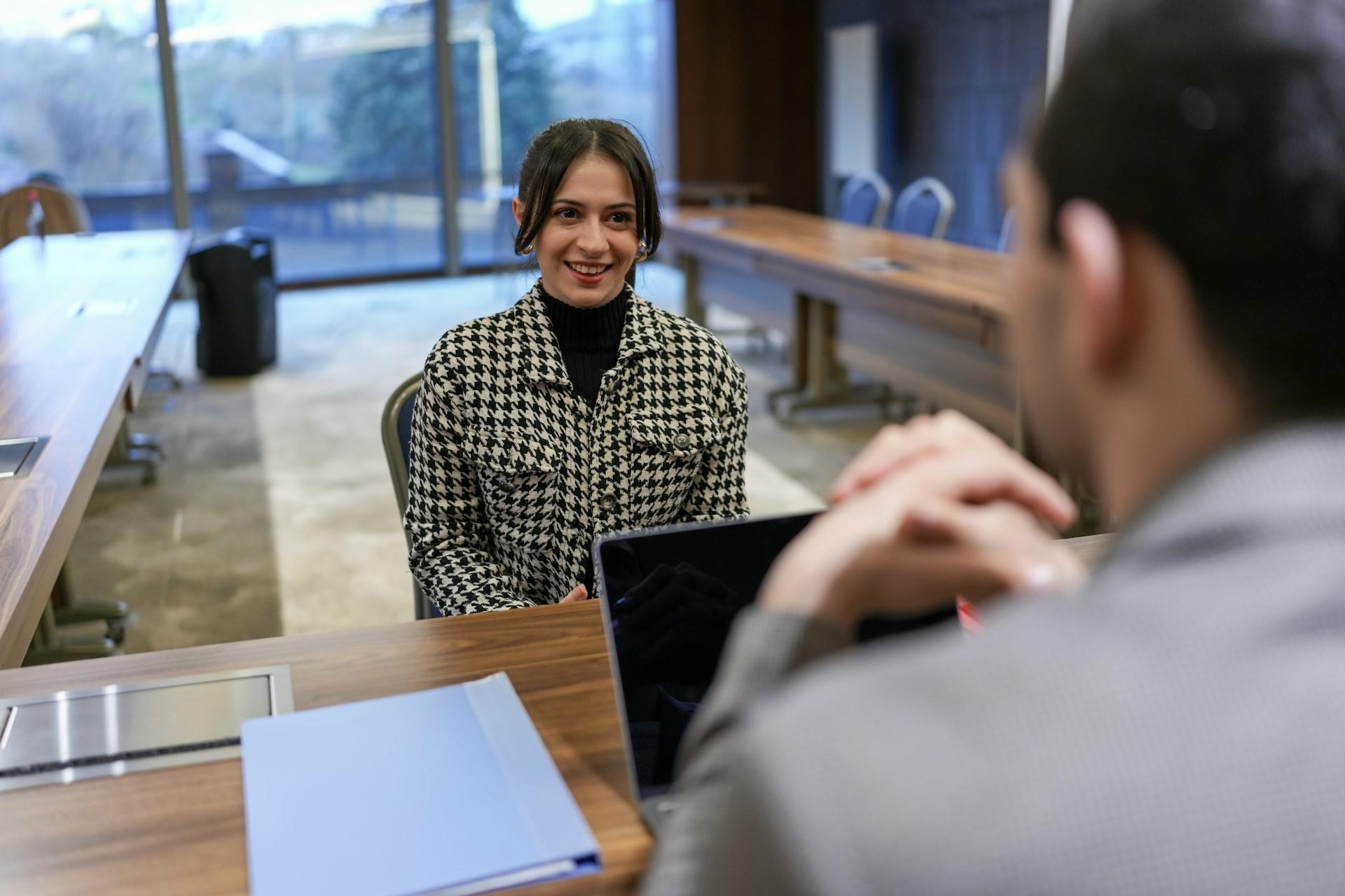A person wearing a houndstooth shirt over a black sweater sits opposite from a person wearing a business suit. 