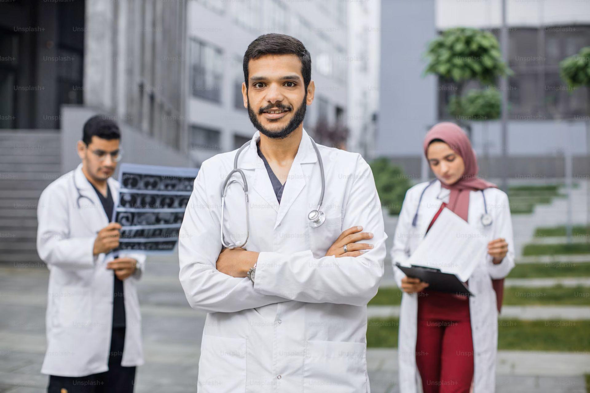 Male doctor in a lab coat with arms crossed with his two medical apprentices.