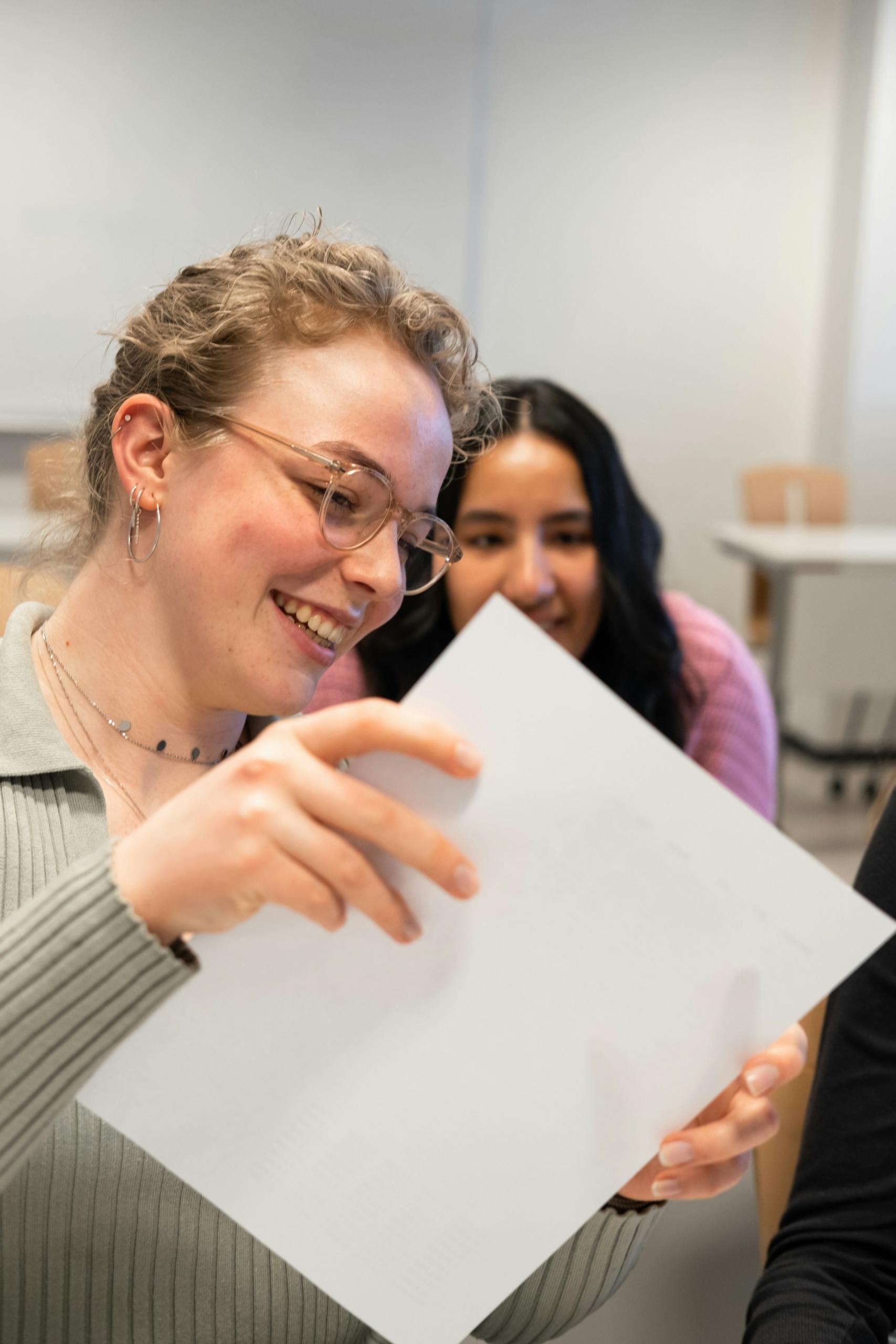 A student smiles as they hold up their paper to show another student their grade. 