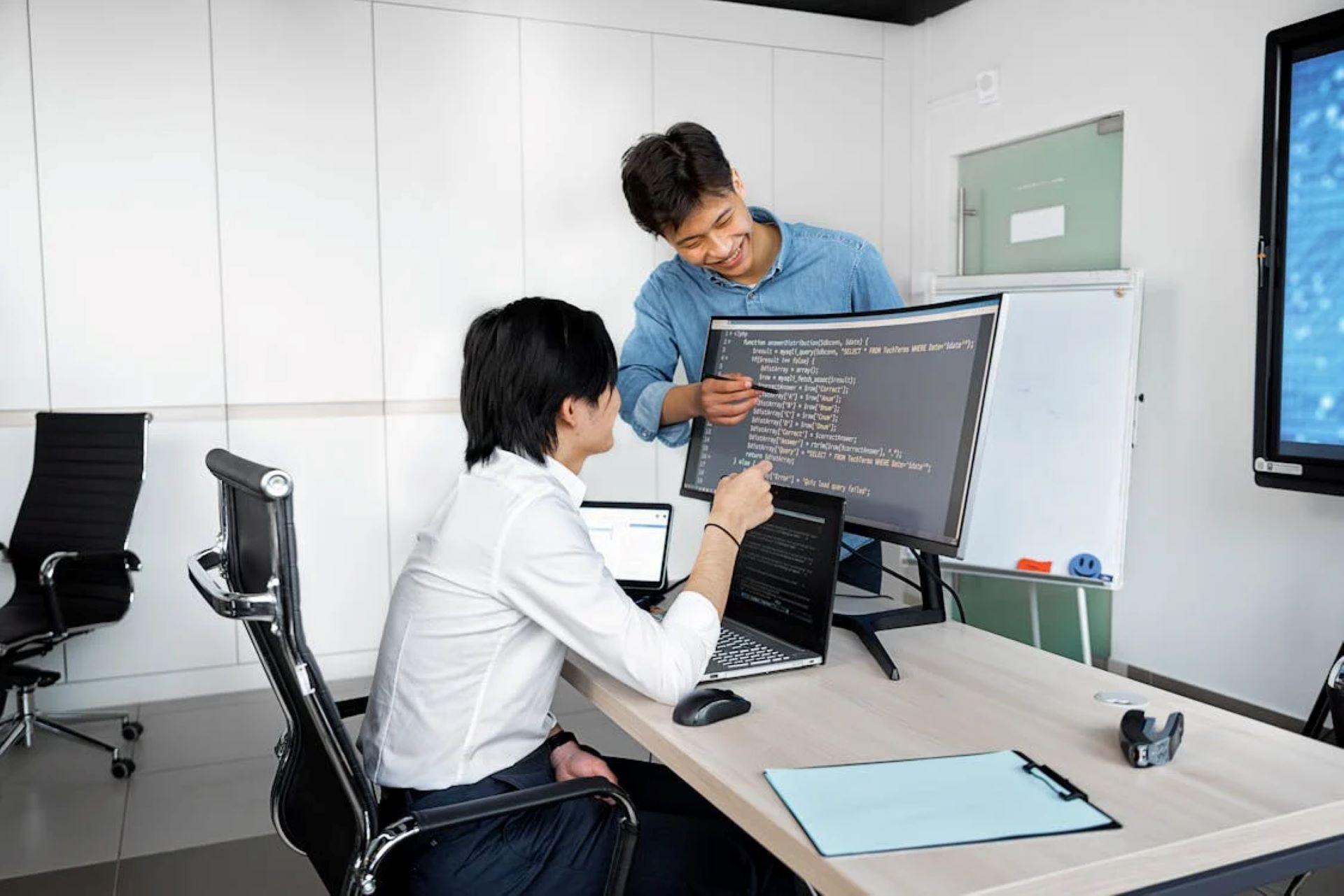 Two men around a computer screen, looking intently at code.