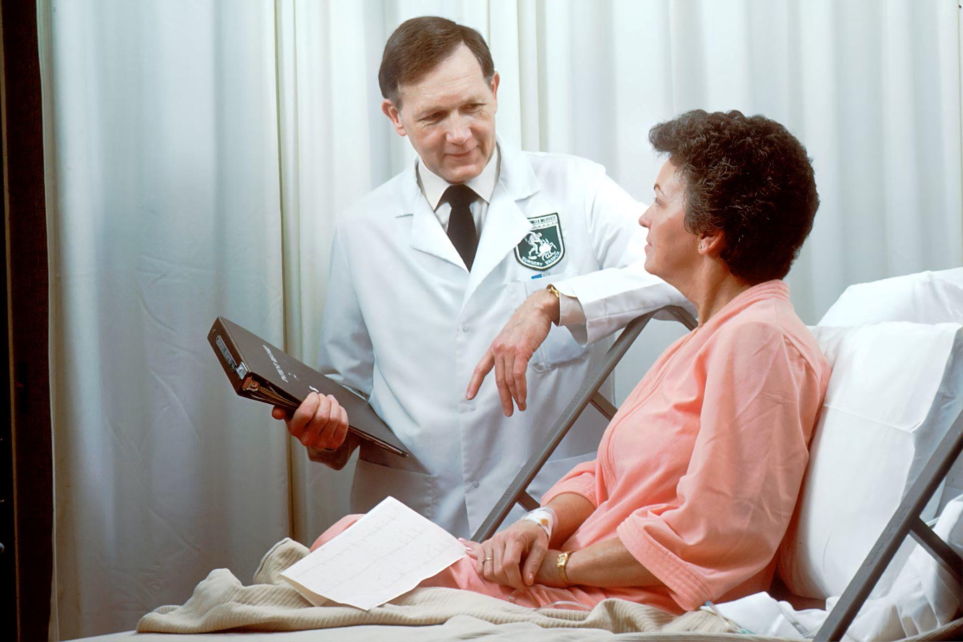 A doctor in a white coat reviews a medical chart with a patient in a hospital bed.