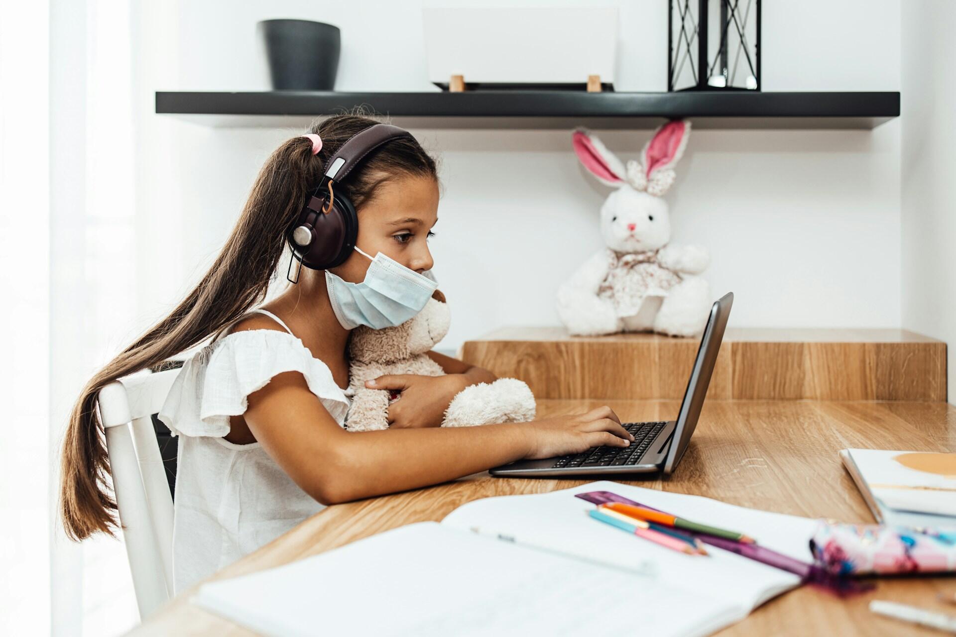 A student wearing a mask sits at a computer.