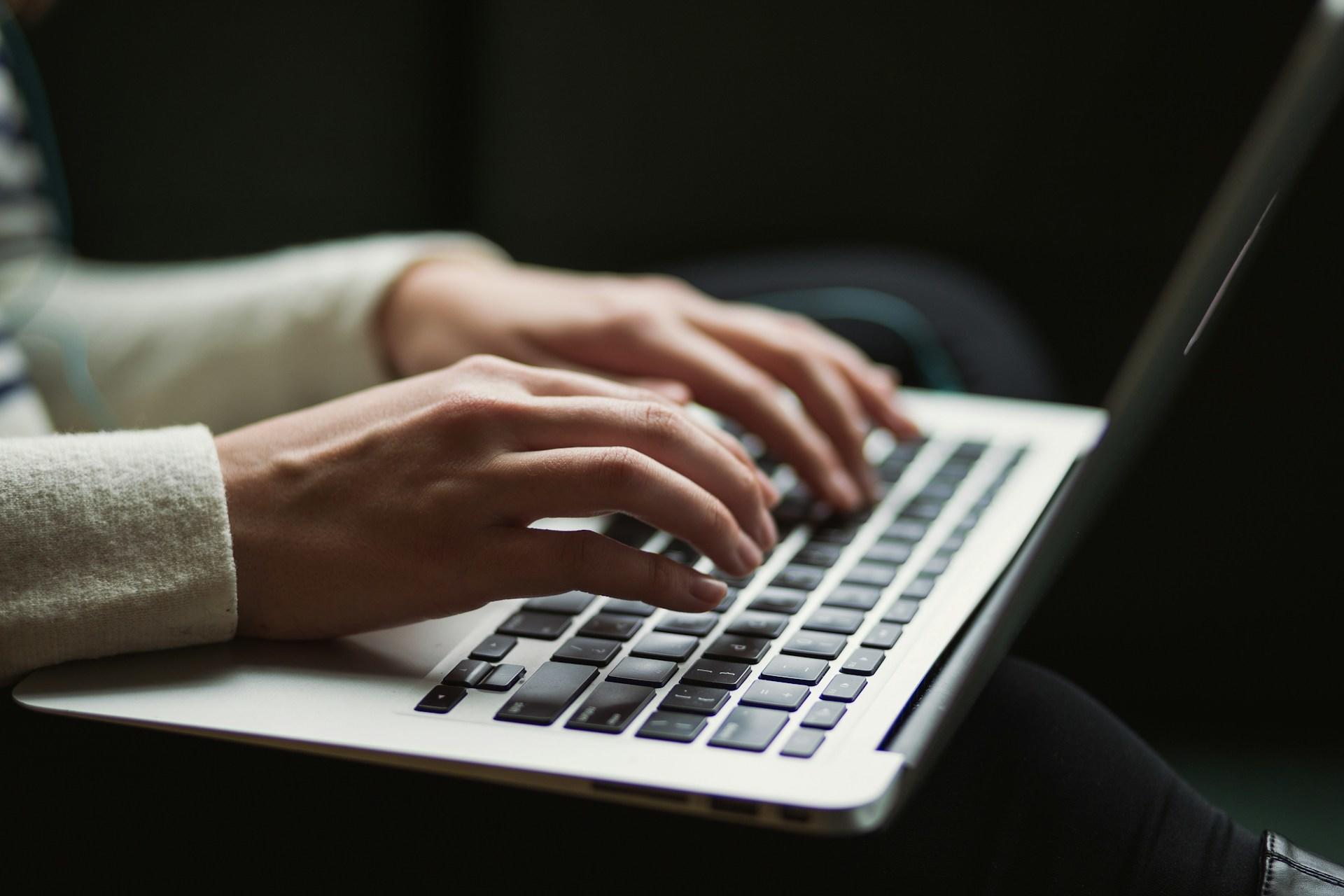 A person's hands typing on a laptop computer.