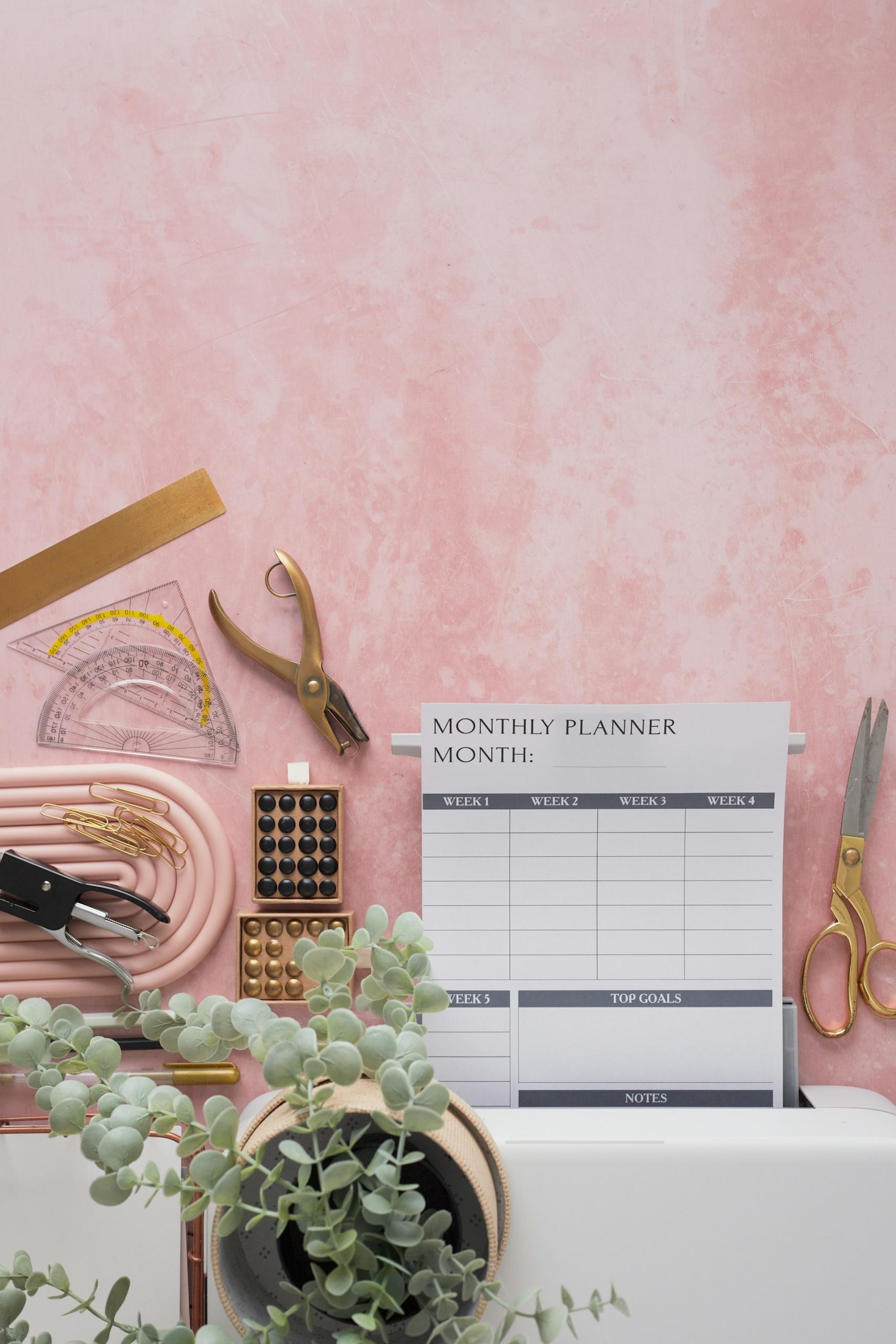 A pink surface, upon which rests various measuring devices and other school supplies, all surrounding a blank monthly planner page. 