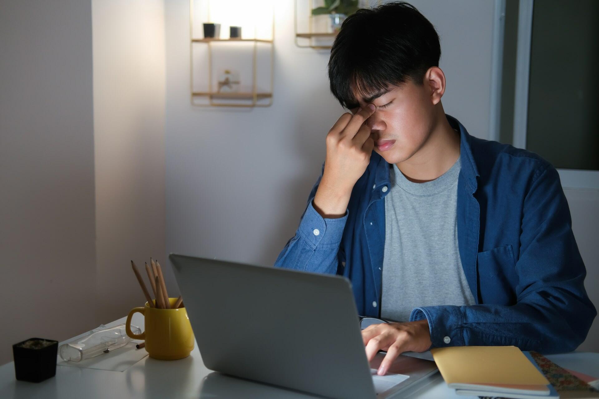 A person in front of a computer, looking stressed.