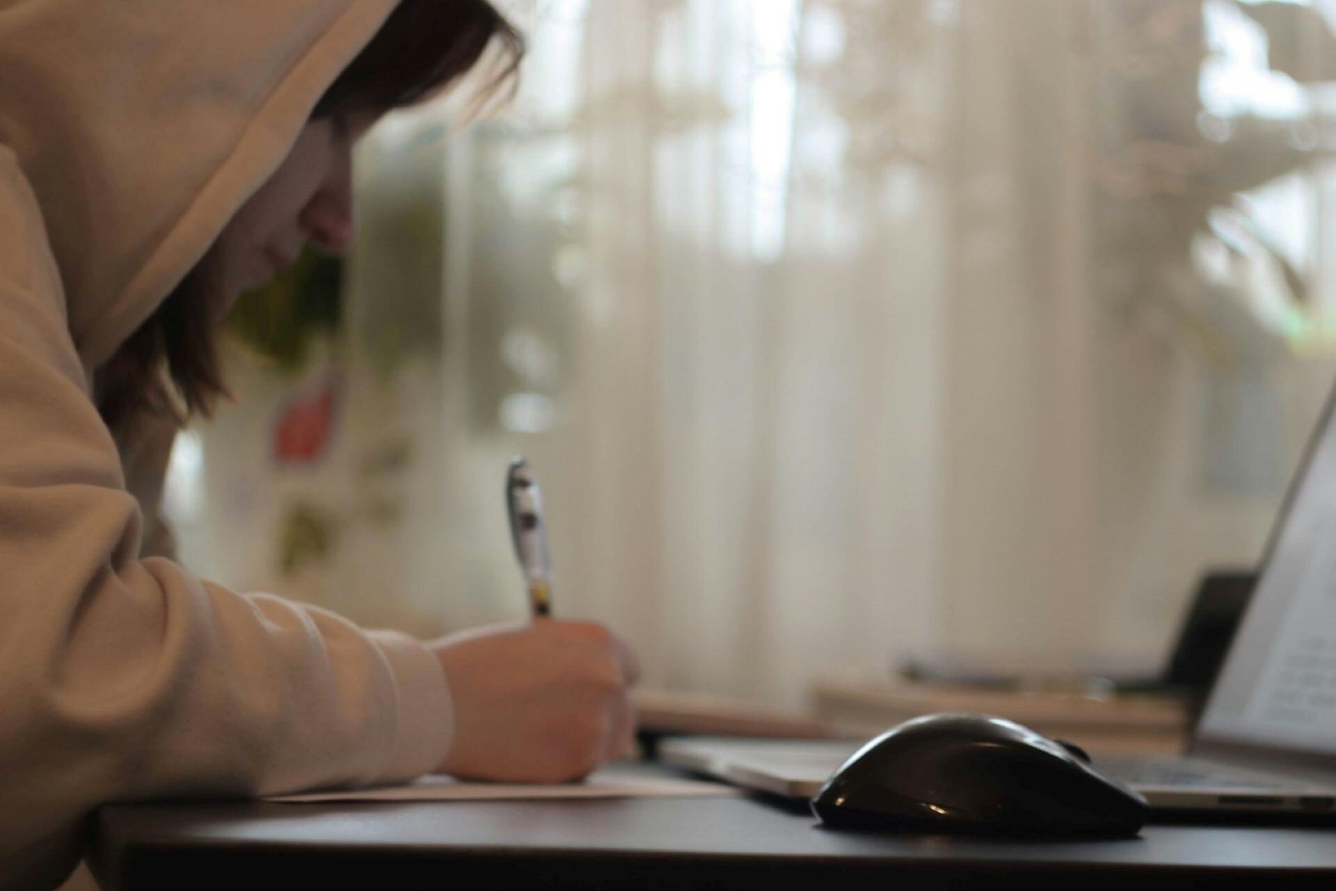 A student looking at a laptop and taking notes.